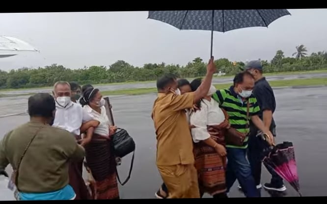 Istri almarhum, Lusia Adinda Leburaya (dipayungi) saat tiba di Bandara Gewayan Flores Timur, Selasa (21/12/2021)