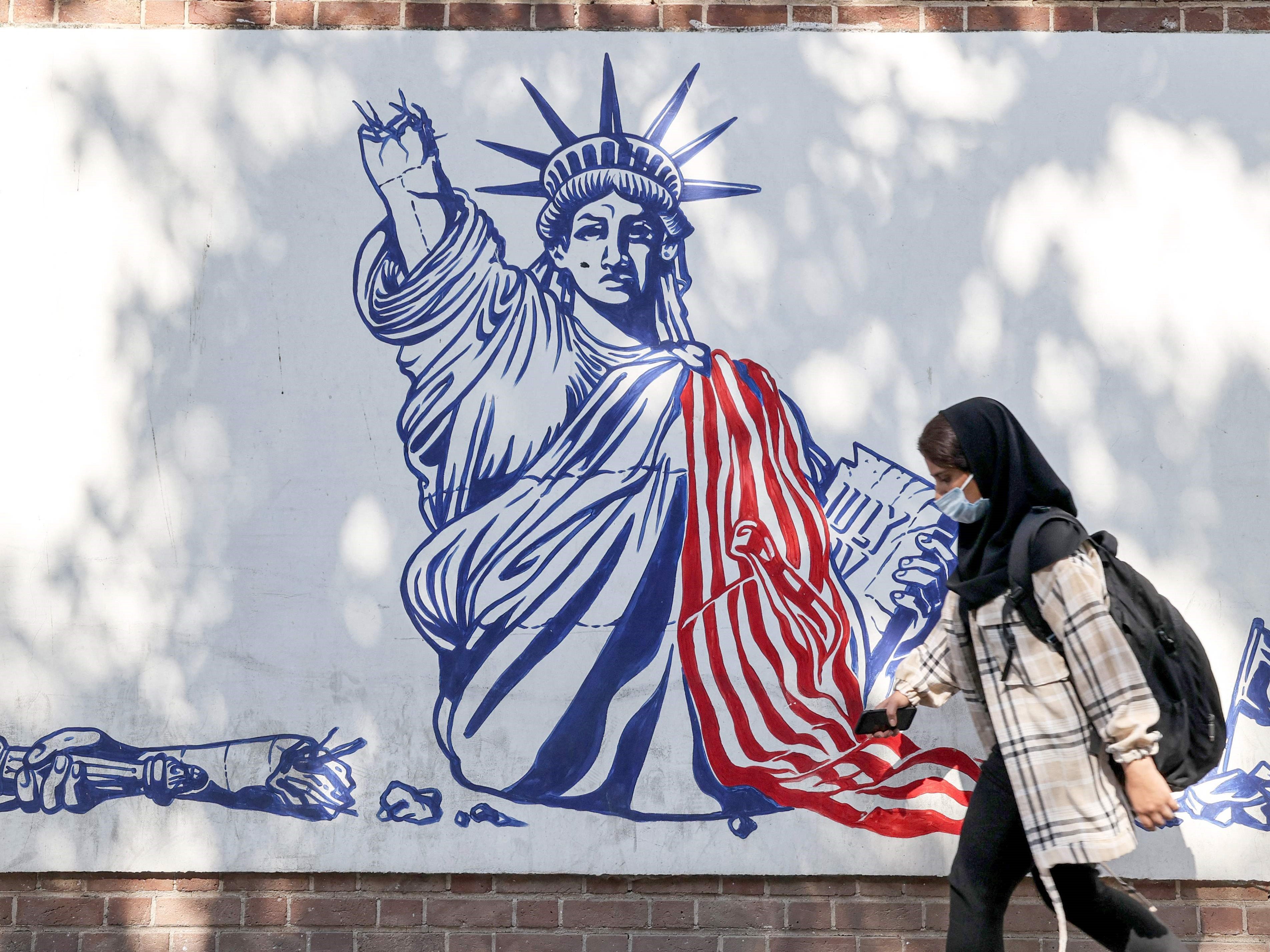 Seorang wanita bermasker melewati mural yang menggambarkan Patung Liberty di Teheran, Iran.