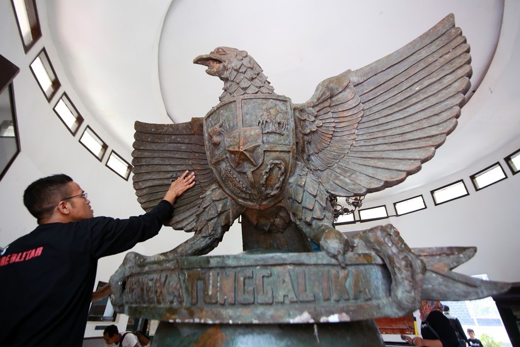 Seorang anggota komunitas pecinta lingkungan membersihkan patung Garuda Pancasila di Museum Candi Penataran, Blitar, Jawa Timur. 