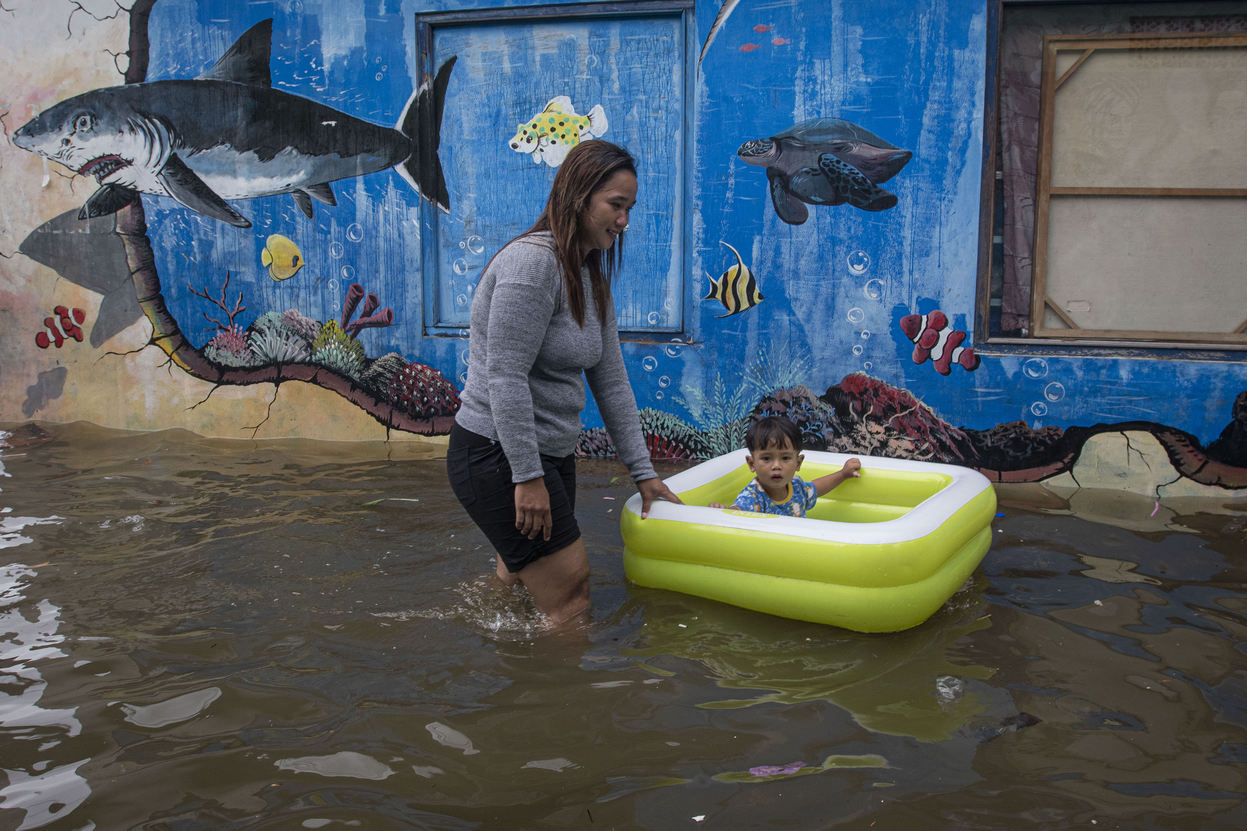 Warga membawa anaknya melintasi banjir pasang air laut atau rob di Kampung Japat, Ancol, Pademangan, Jakarta.