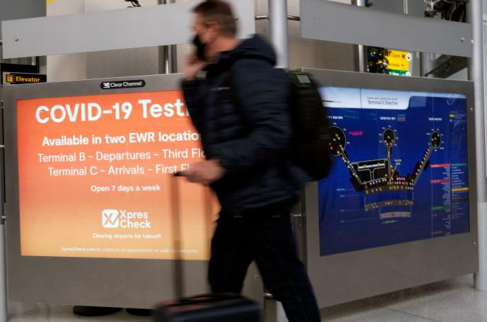 Seorang pelancong melintas di depan papan pengumuman uji covid-19 di Bandara Internasional Liberty di Newark, AS. 