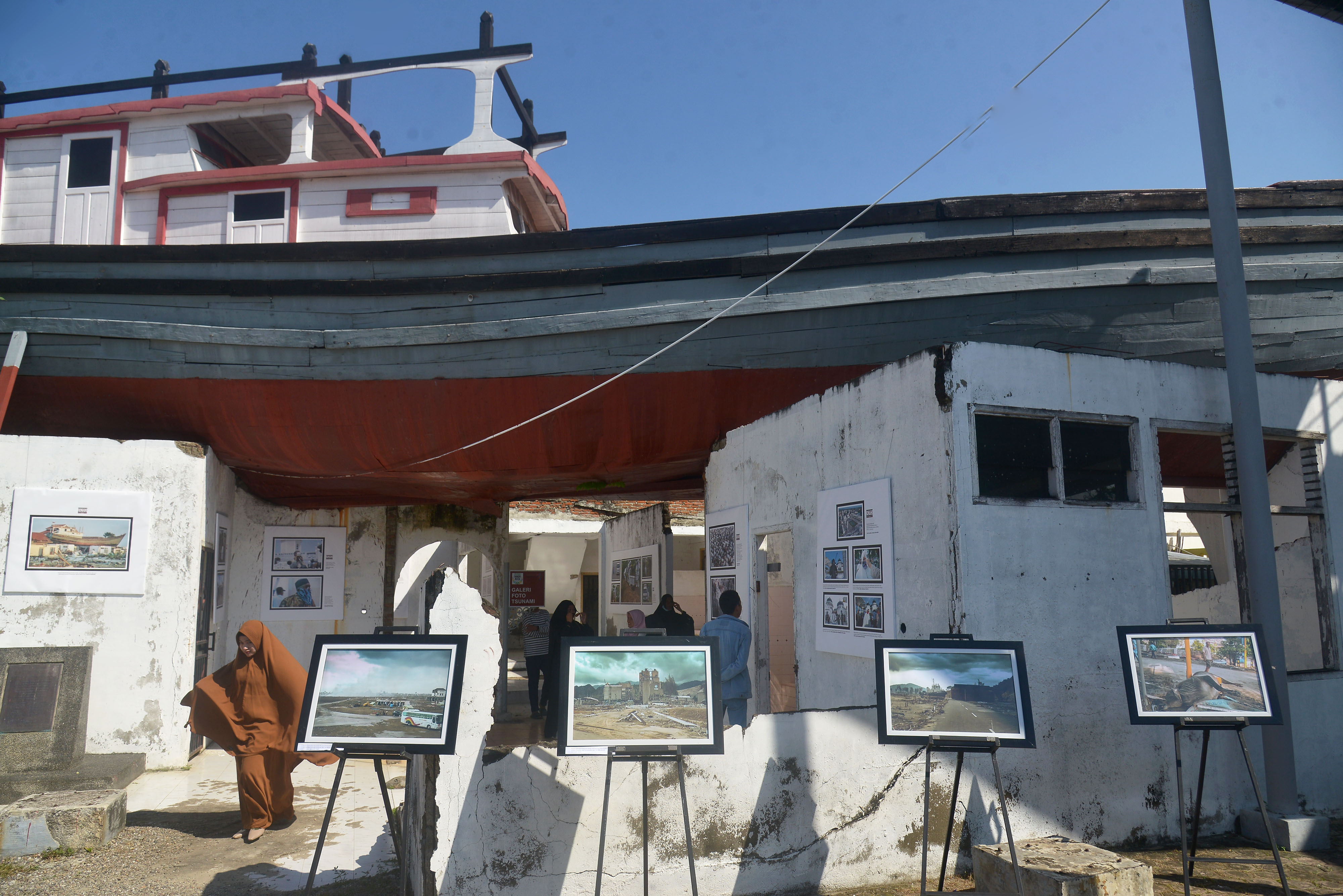 Pengunjung menyaksikan pameran foto Tsunami Pandemi di situs tsunami Kapal Atas Rumah, Desa Lampulo, Banda Aceh, Aceh, Sabtu (25/12/2021)