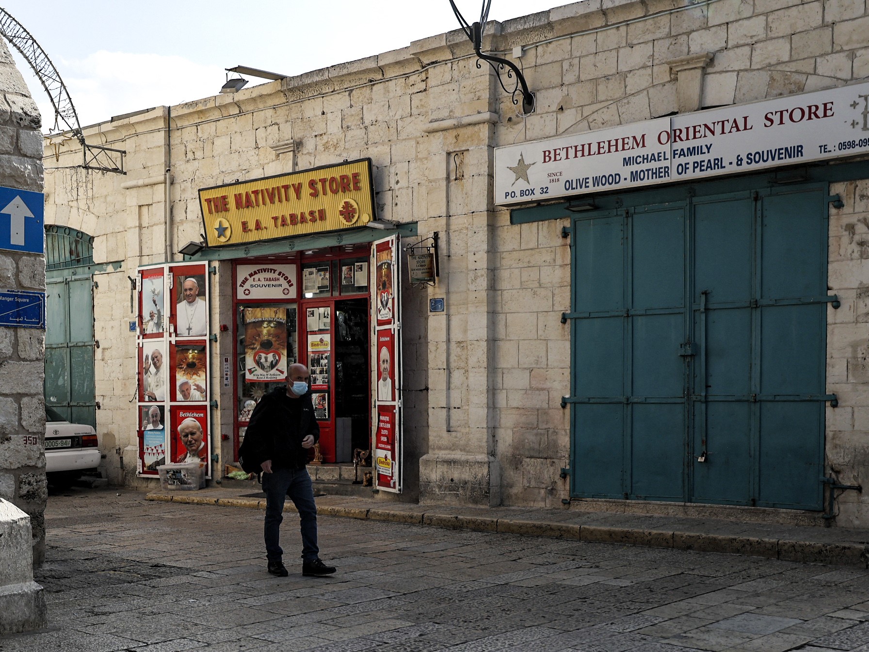 Seorang pria berjalan melewati toko-toko yang tutup di Manger Square yang kosong di luar Church of the Nativity.