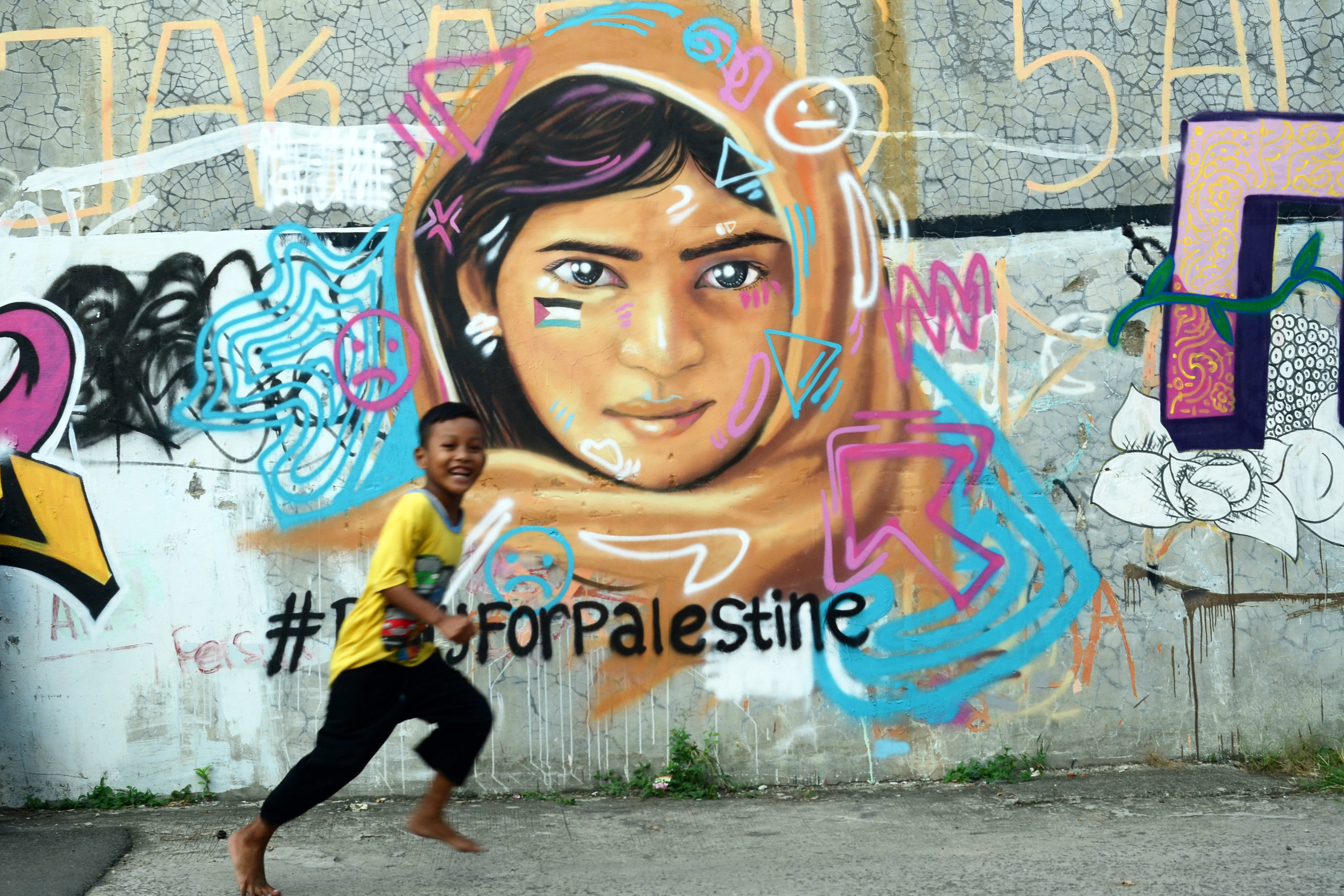 Seorang anak melintas di depan mural bertema Palestina di Bekasi, Jawa Barat, Kamis (3/6/2021). 