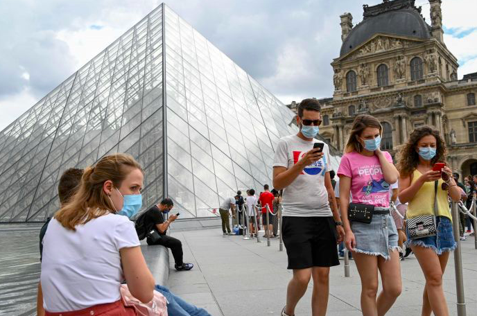 Warga mengenakan masker melintas di depan Pyramide du Louvre di Paris, Prancis.