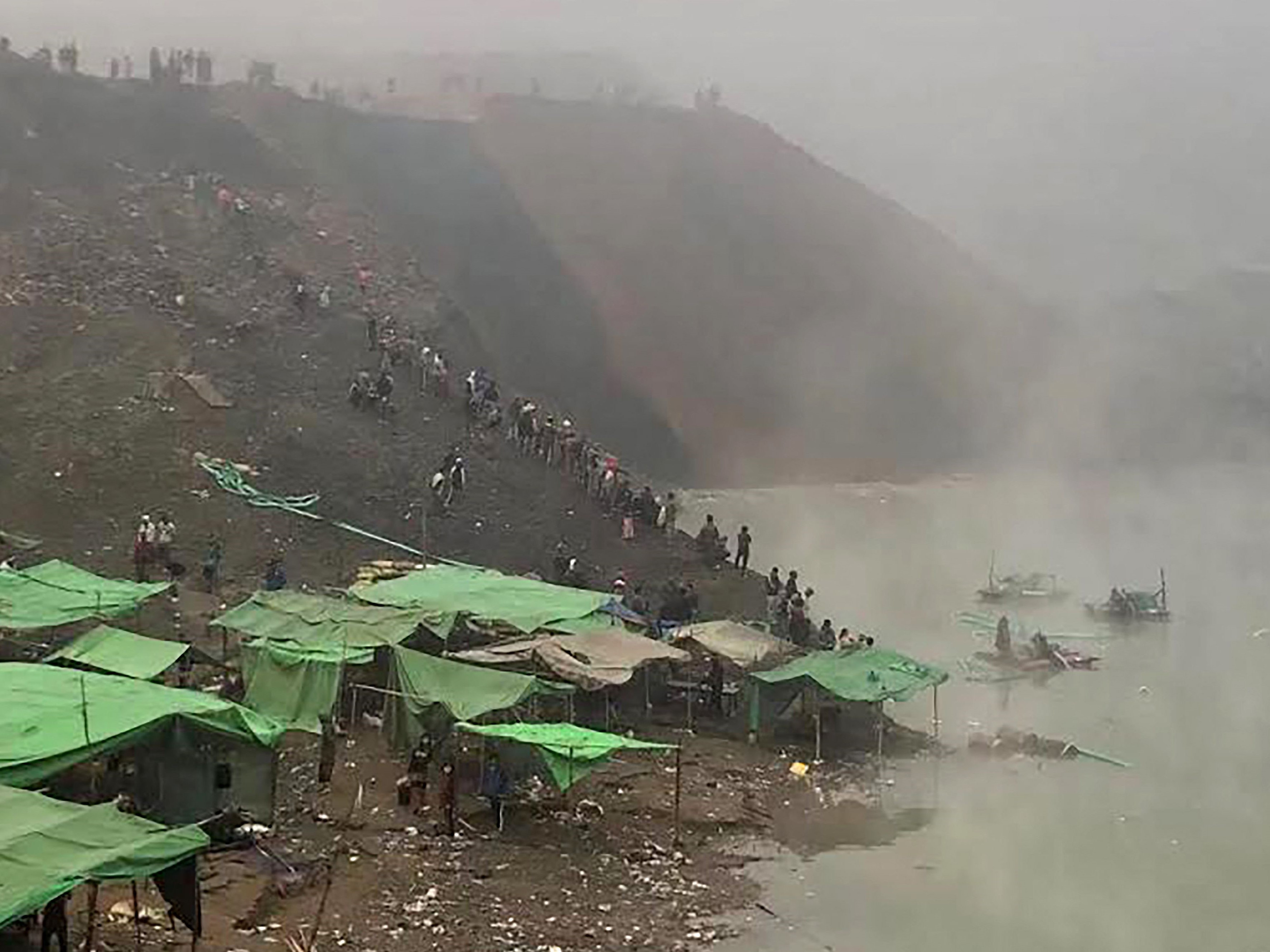 Orang-orang menyaksikan tim penyelamat bersiap untuk mencari penambang yang hilang setelah tanah longsor di tambang batu giok di Hpakant.