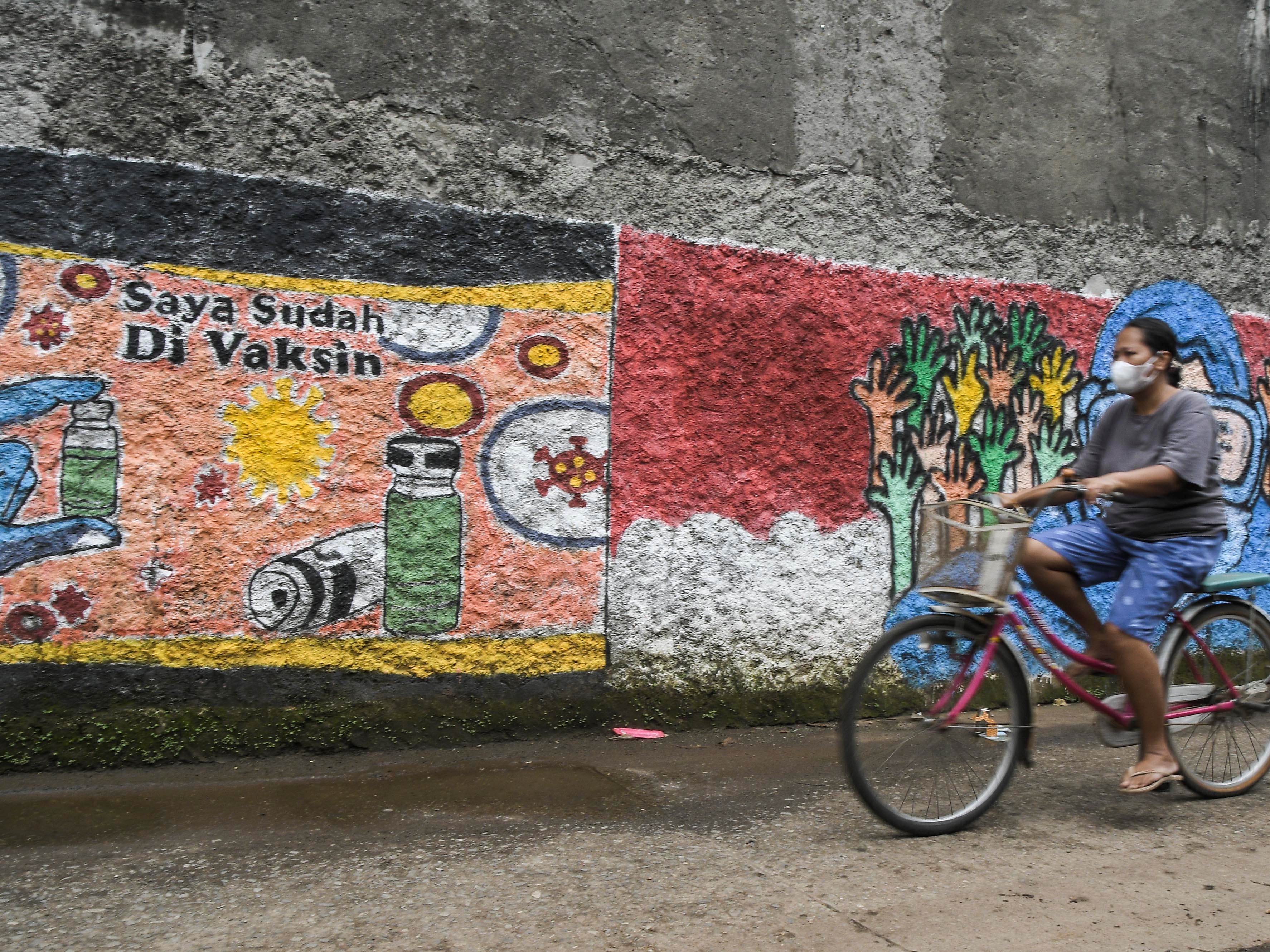 Pengendara sepeda melintasi mural bertemakan sosialisasi untuk vaksinasi covid-19 di Bekasi, Jawa Barat, Senin (15/11/2021). 