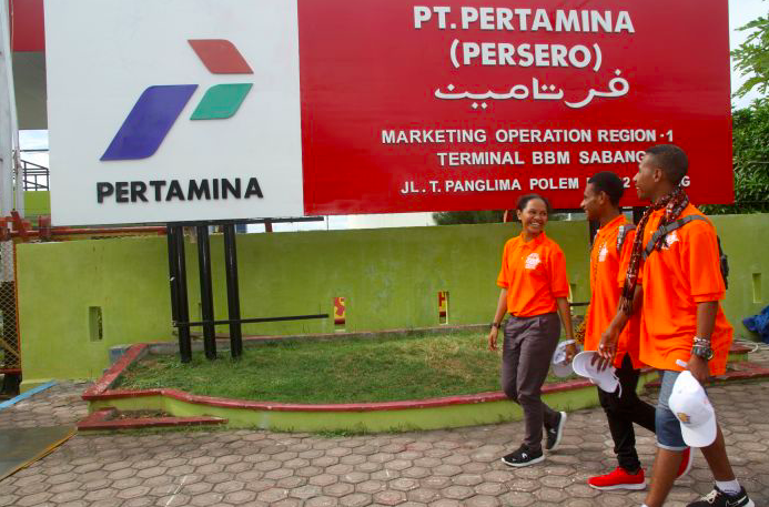 Sejumlah pelajar asal Papua melintas di depan logo PT Pertamina usai berkunjung ke Terminal Bahan Bakar Minyak Sabang, Aceh.