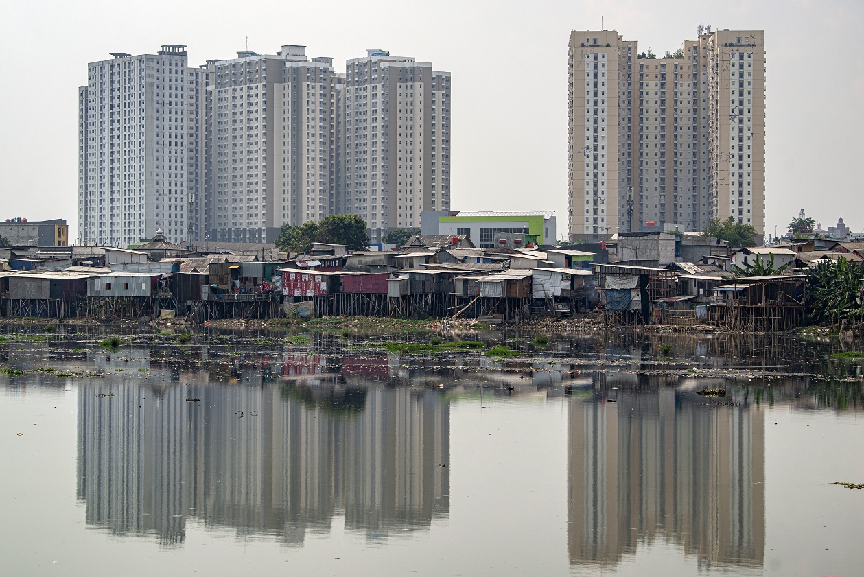 Bangunan semi permanen hunian warga berdiri dengan latar belakang gedung apartemen di tepi Waduk Pluit, Penjaringan, Jakarta.