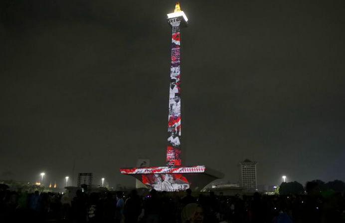 Pengunjung menyaksikan pertunjukan video mapping malam tahun baru di Monas, Jakarta, Selasa (31/12) malam.