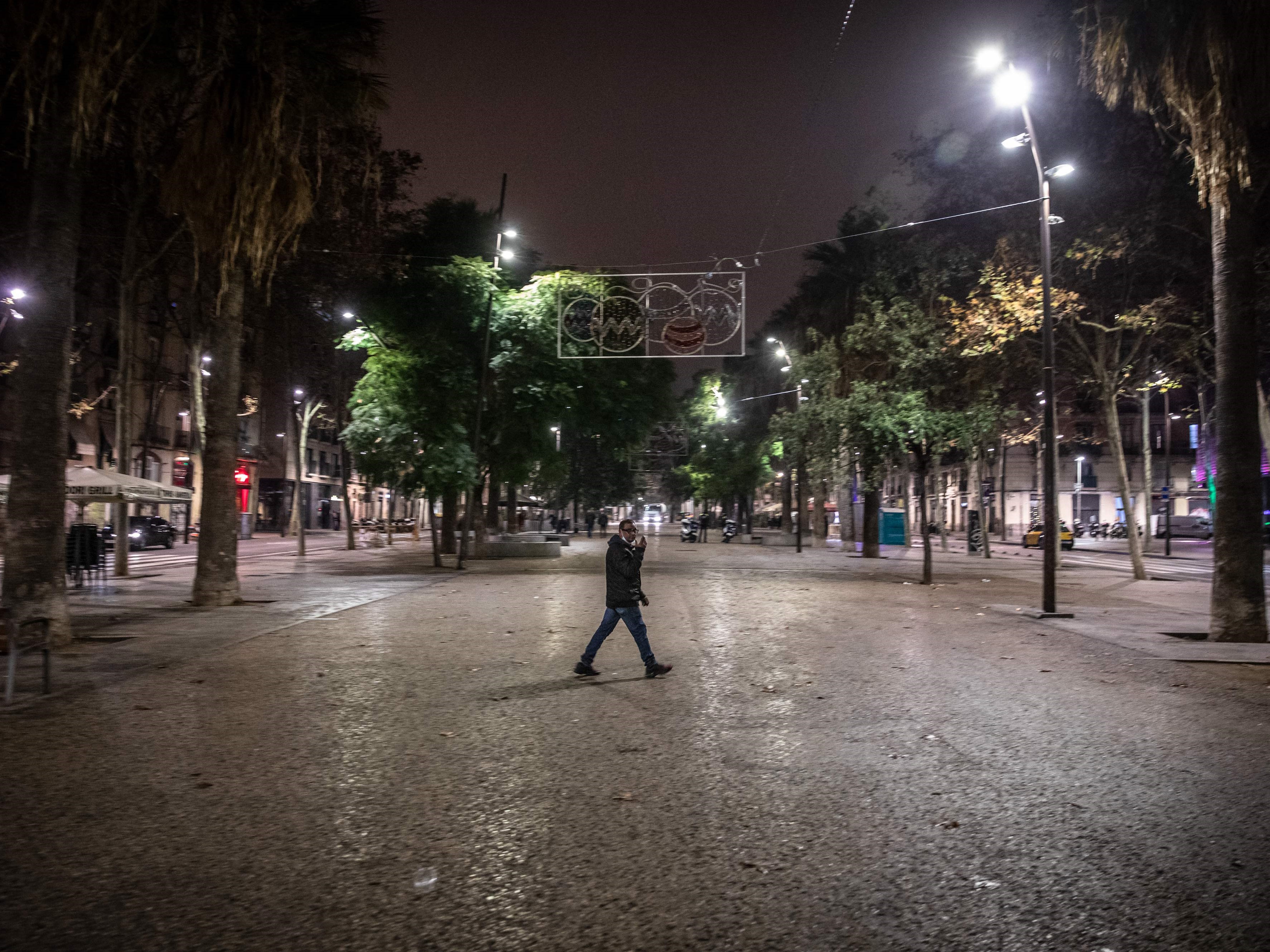 Seorang pejalan kaki berjalan di jalan tengah kosong La Rambla, Barcelona, ​​pada malam 23 Desember hingga 24 Desember 2021.