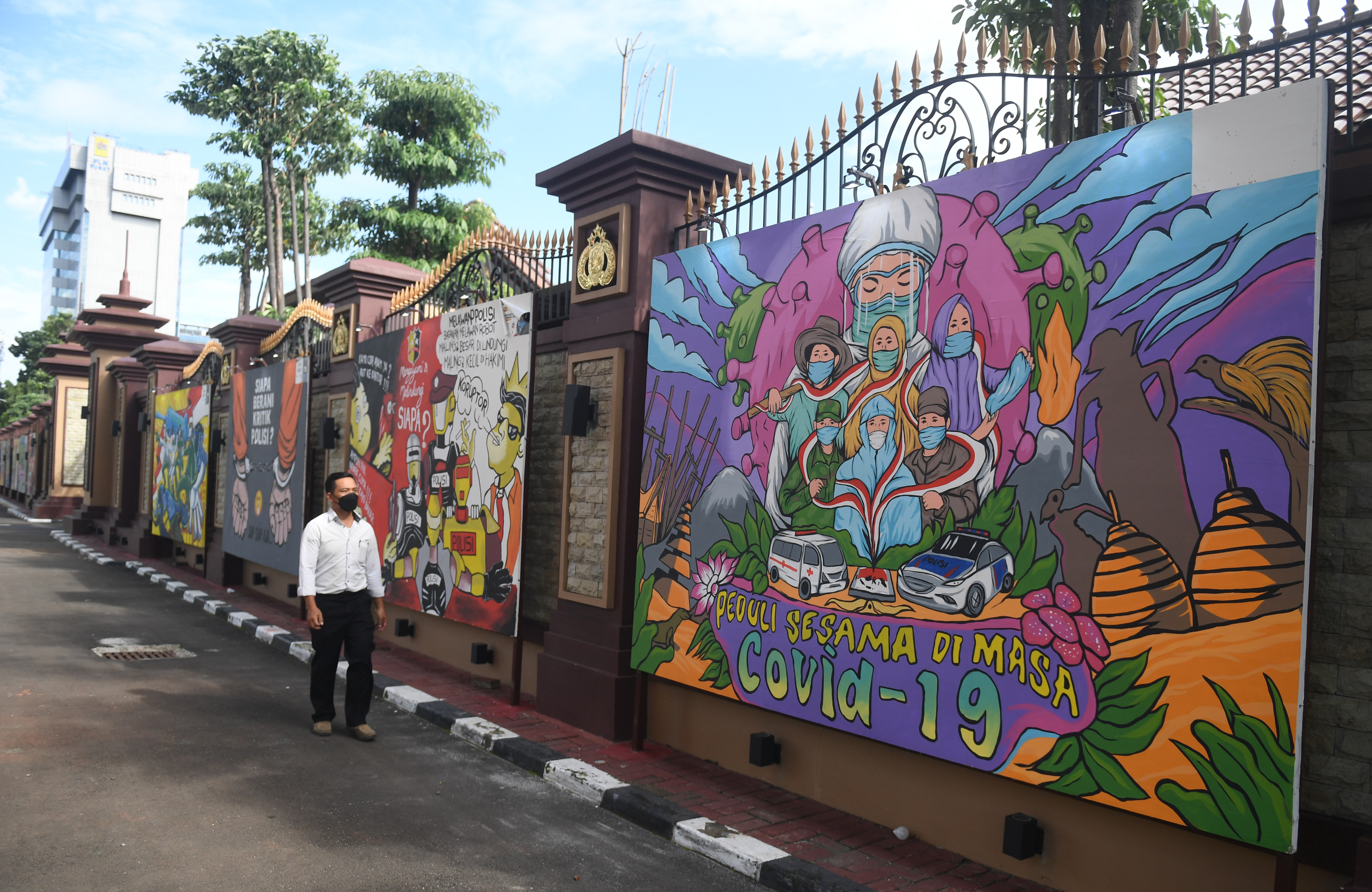 Warga melintas di dekat mural bertema covid-19 di Jakarta.