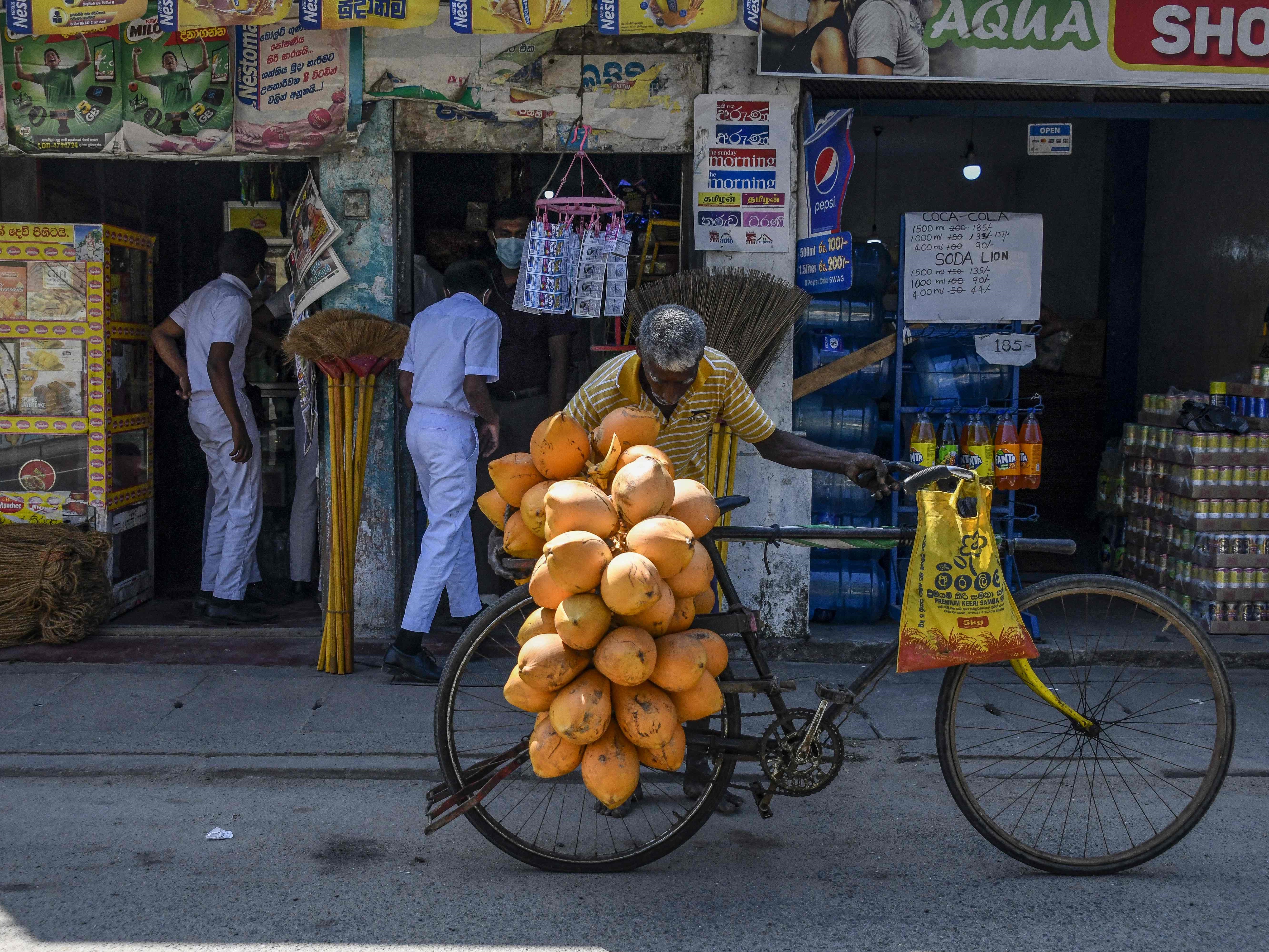 Seorang pedagang yang menjual kelapa menyesuaikan sepedanya di depan sebuah toko di Galle, Sri Lanka.