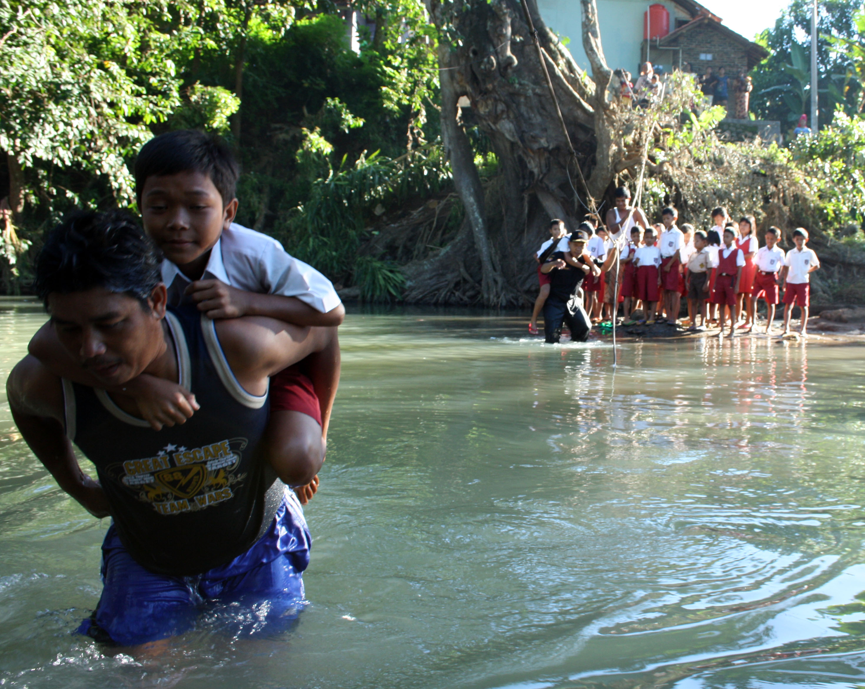 Seorang siswa SD digendong saat menyeberangi sungai menuju ke sekolah
