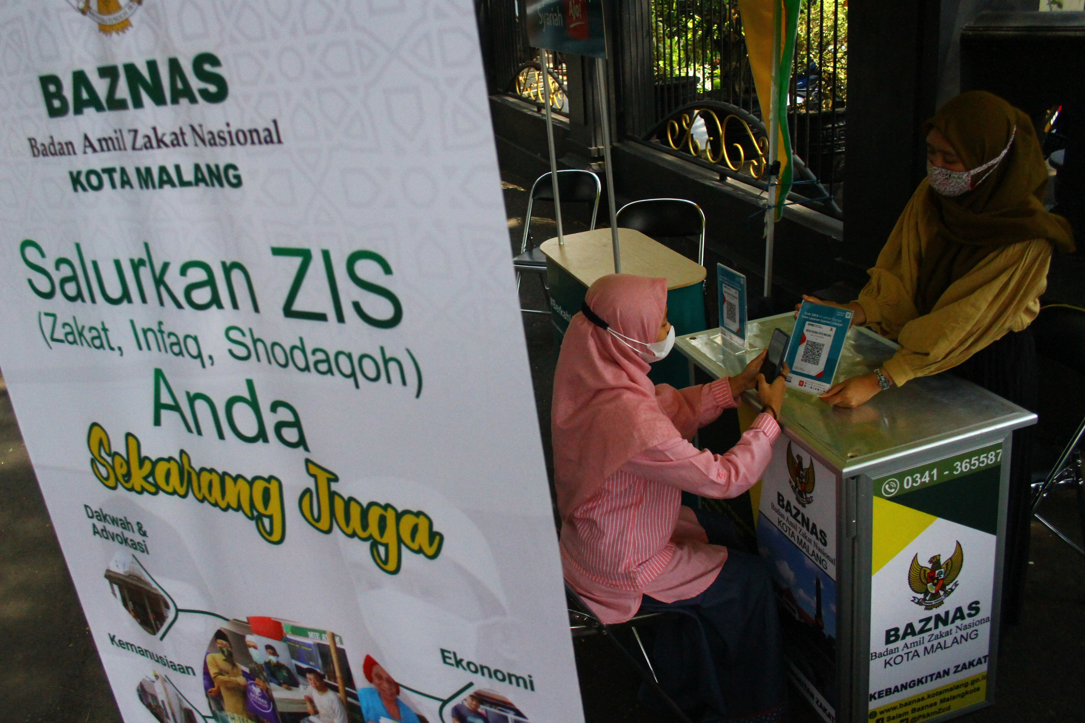 Relawan Baznas membantu warga membayar zakat secara digital melalui kode quick respons (QR), di Malang, Jawa Timur, Selasa (4/5/2021).