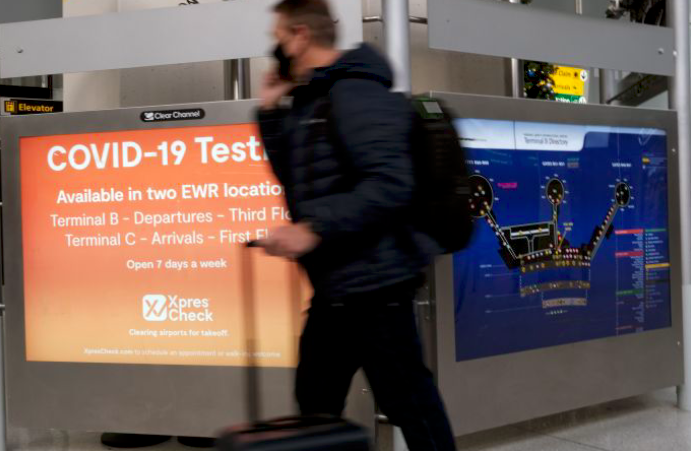 Seorang pelancong melintas di depan papan pengumuman uji covid-19 di Bandara Internasional Liberty di Newark, AS.
