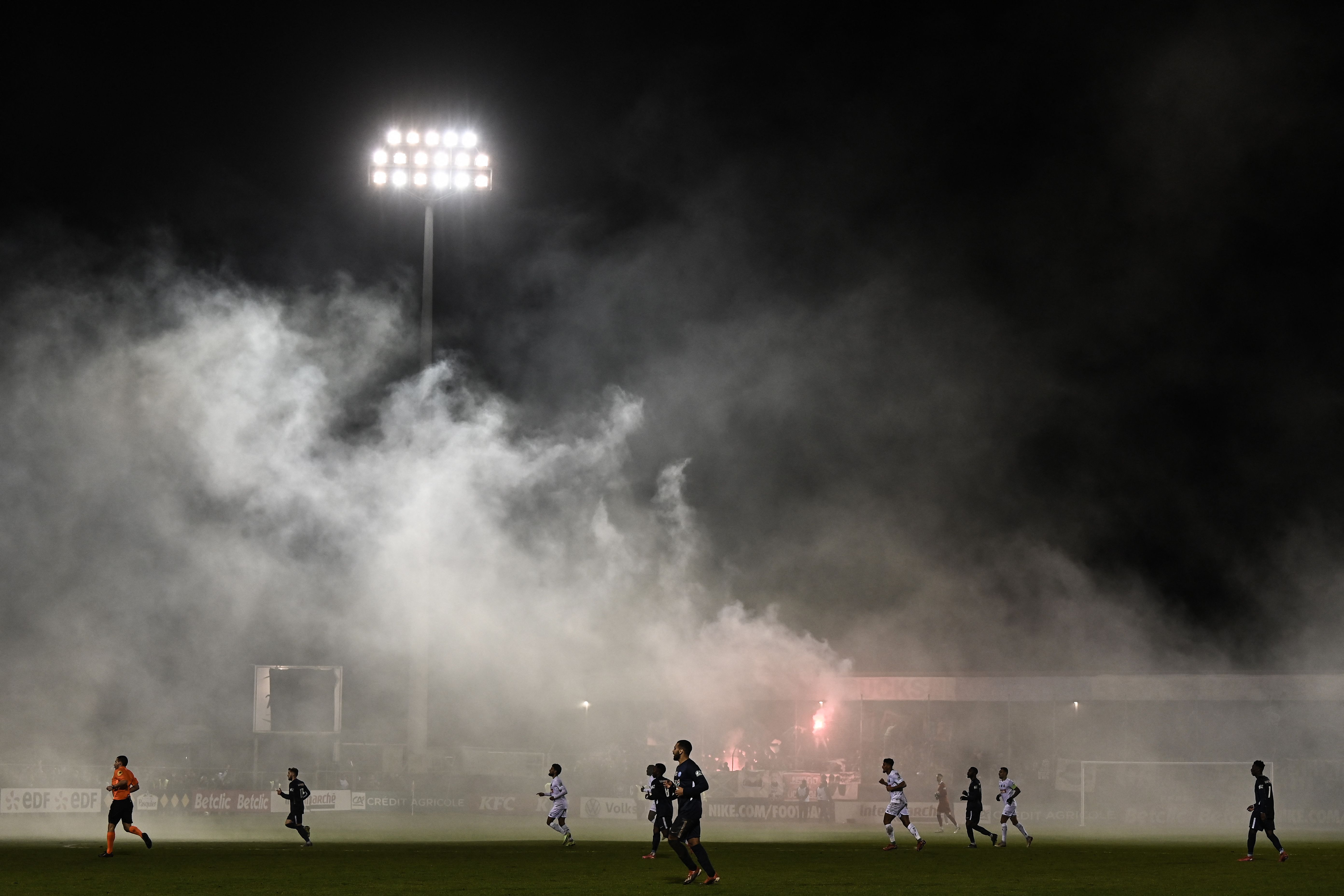 Asap memenuhi stadion dari petasan yang dilemparkan pendukung dalam laga Cope de France antara Jura Sud dan Saint-Etienne.