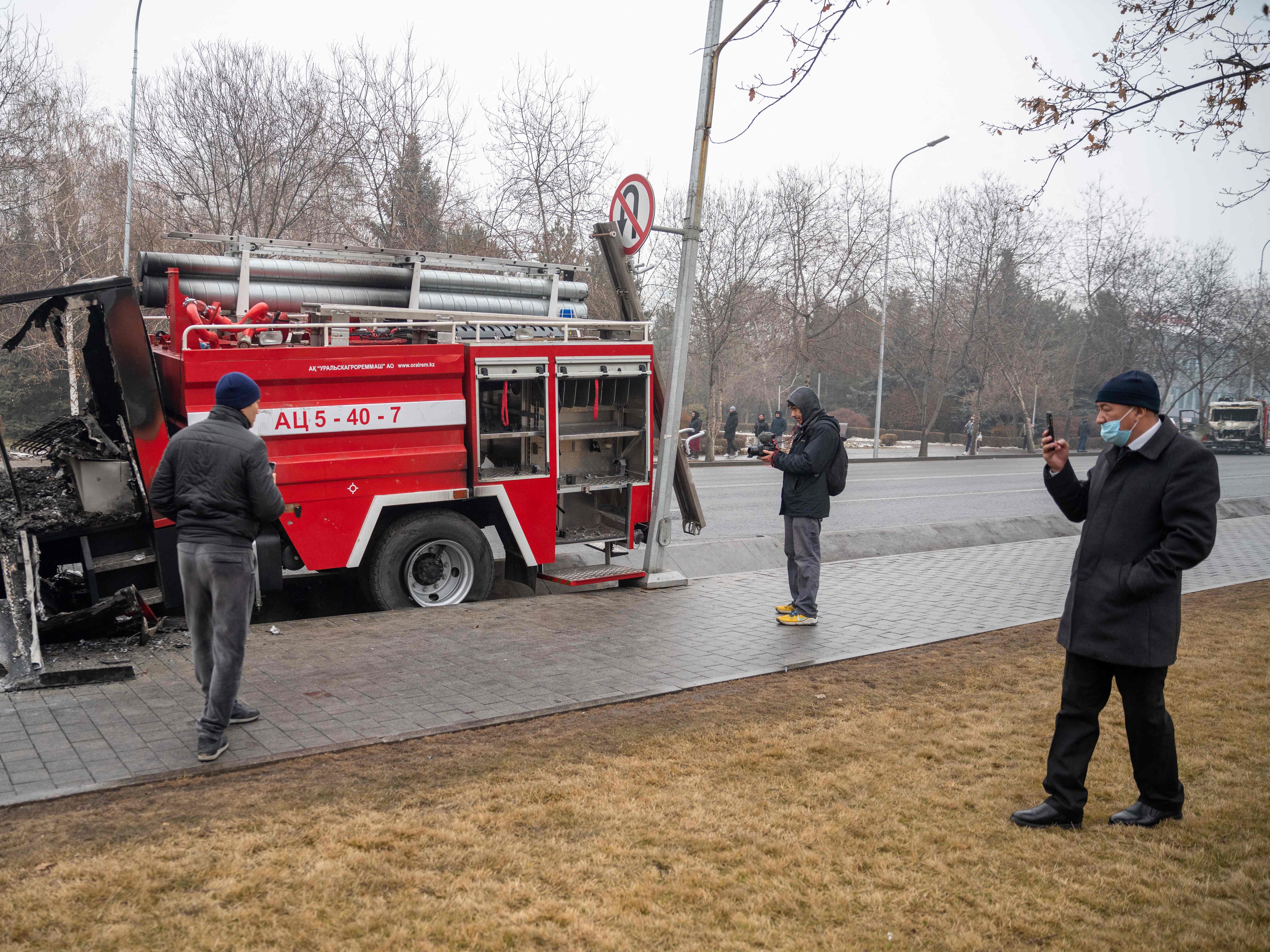 Orang yang lewat mengambil gambar mobil pemadam kebakaran yang terbakar di pusat Almaty pada 7 Januari 2022 akibat kerusuhan.