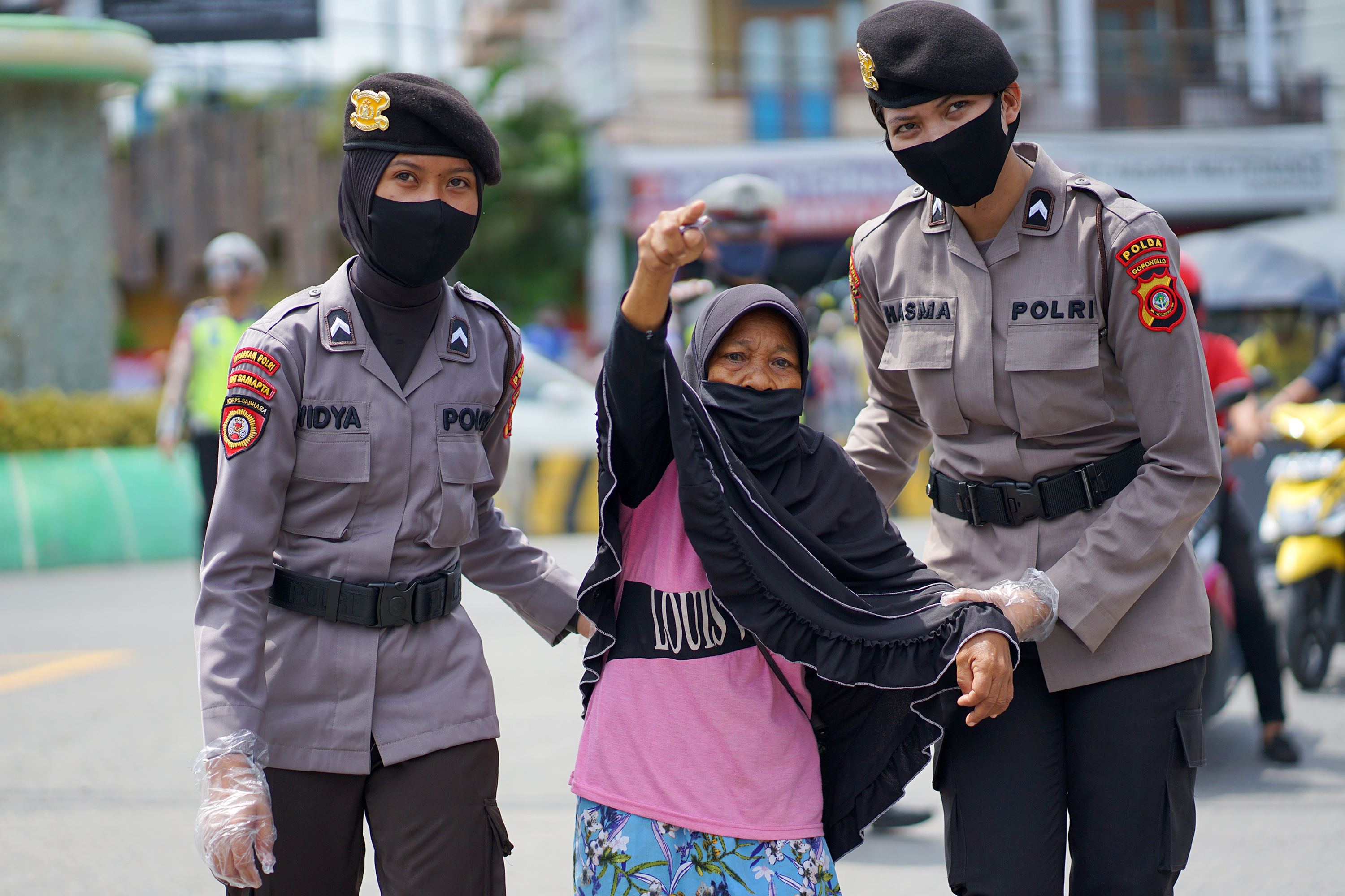 Sejumlah polisi wanita (polwan) menuntun seorang nenek menyeberang jalan saat pembagian masker gratis di Kota Gorontalo.