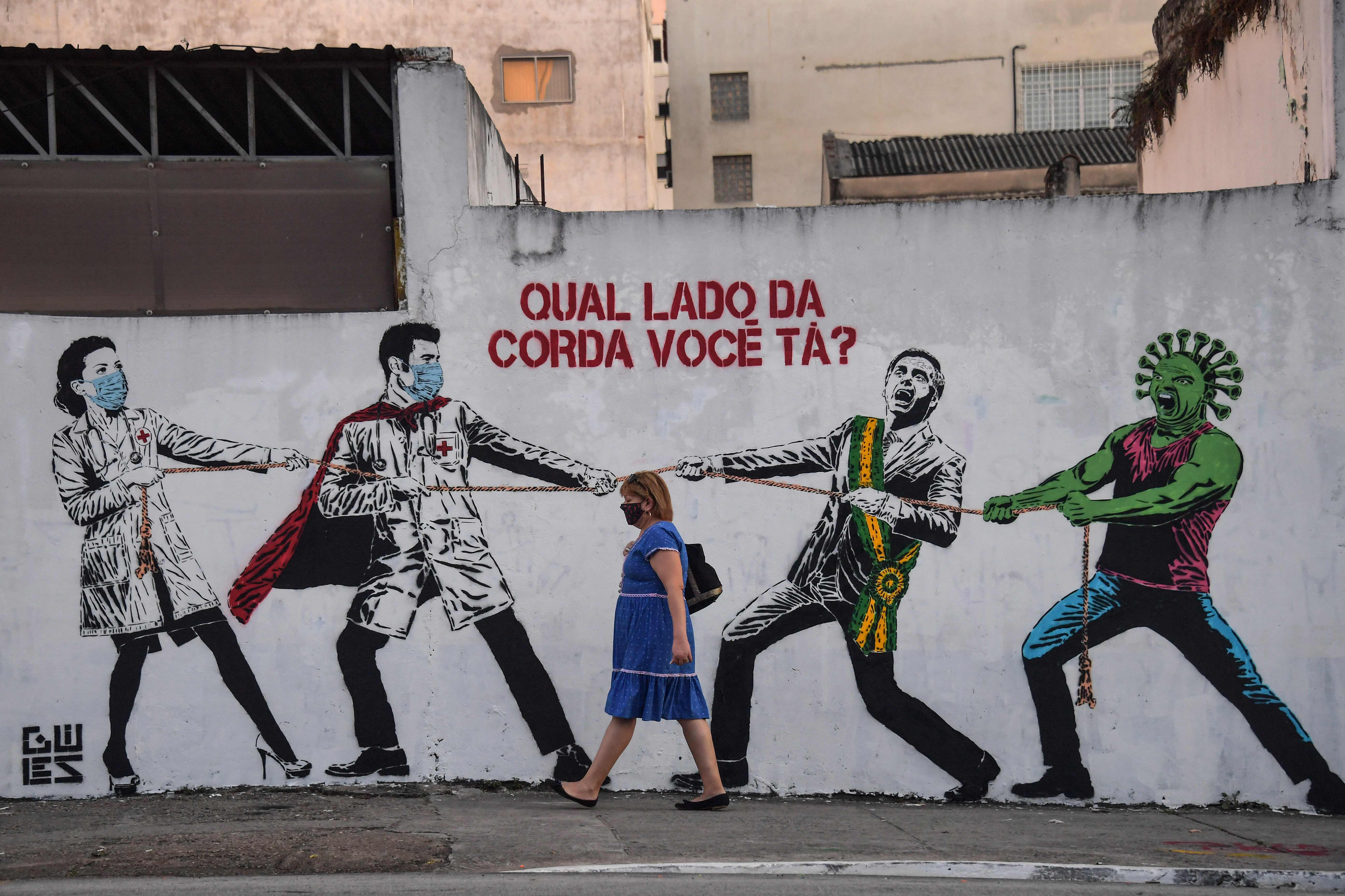 Warga berjalan di depan mural yang menggambarkan Presiden Brasil Jair Bolsonaro menolak penanganan Covid-19 yang dilakukan Ilmuwan negaranya