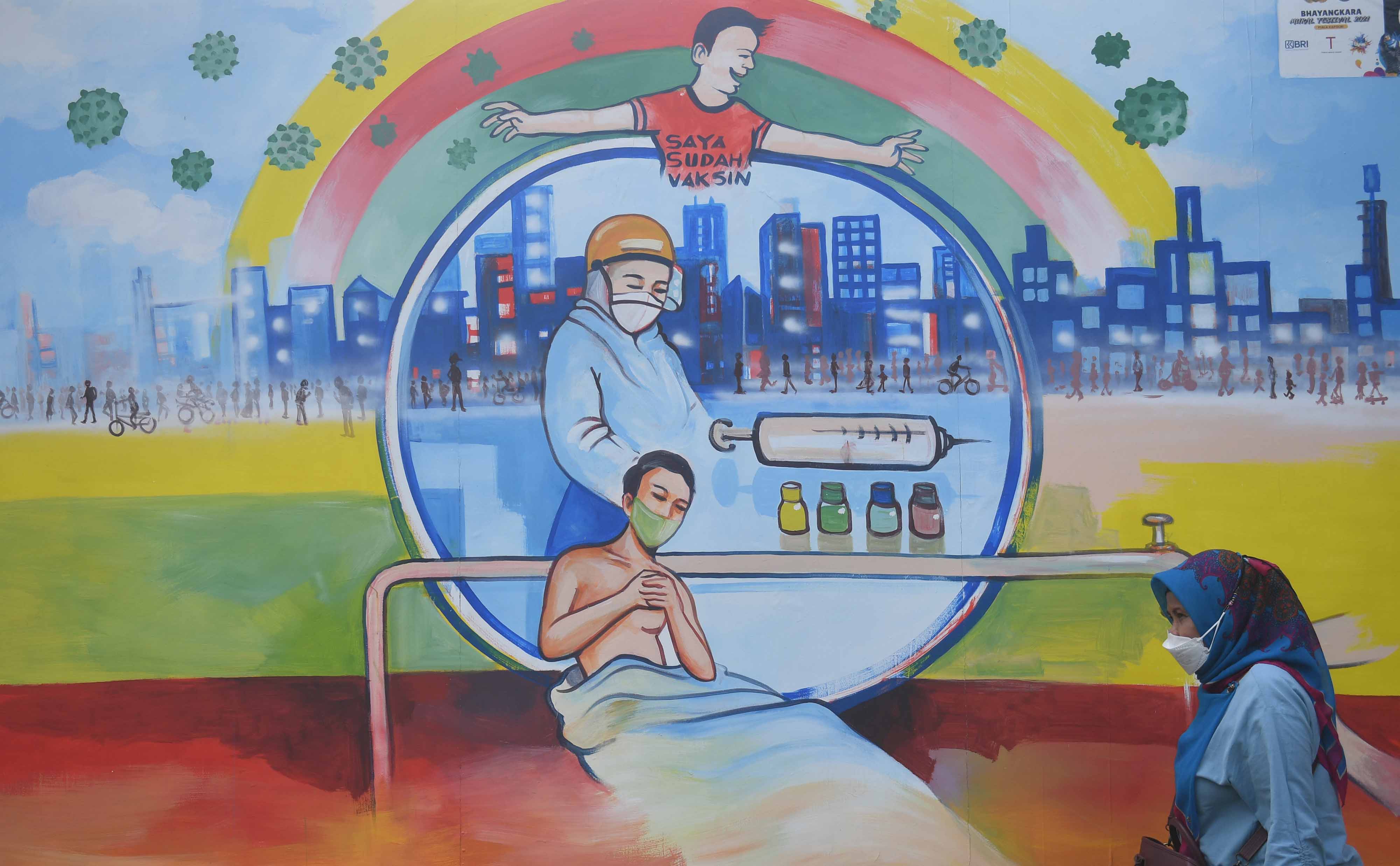 Warga melintas di dekat mural bertema covid-19 di Jakarta.