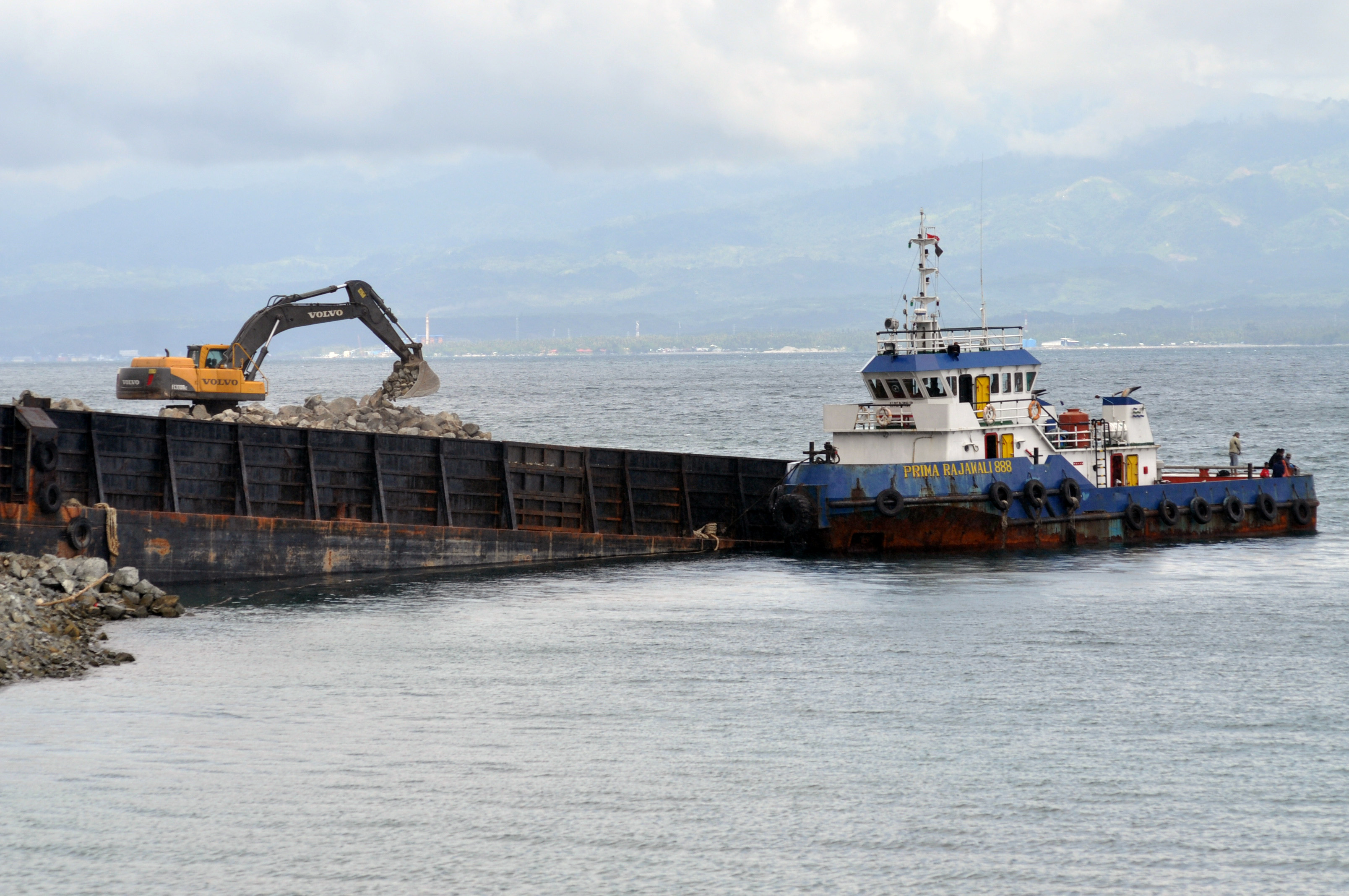 Alat berat memasukkan hasil tambang berupa batu ke dalam tongkang di Kawasan Pertambangan di Palu, Sulawesi Tengah.