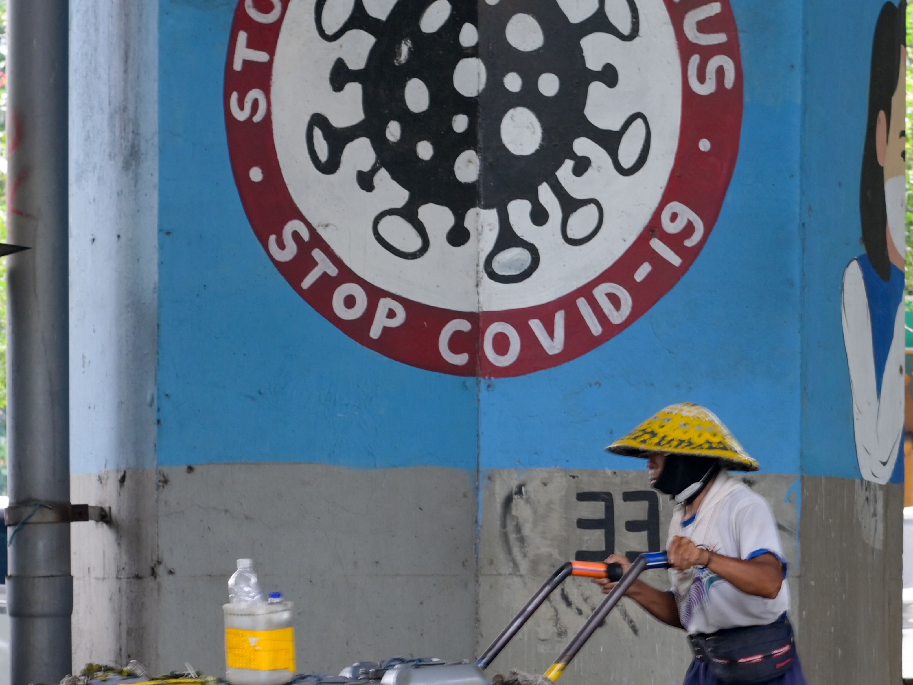 Seorang pedagang berjalan melewati tiang dengan mural melawan covid-19 di Jakarta pada 13 Januari 2022.