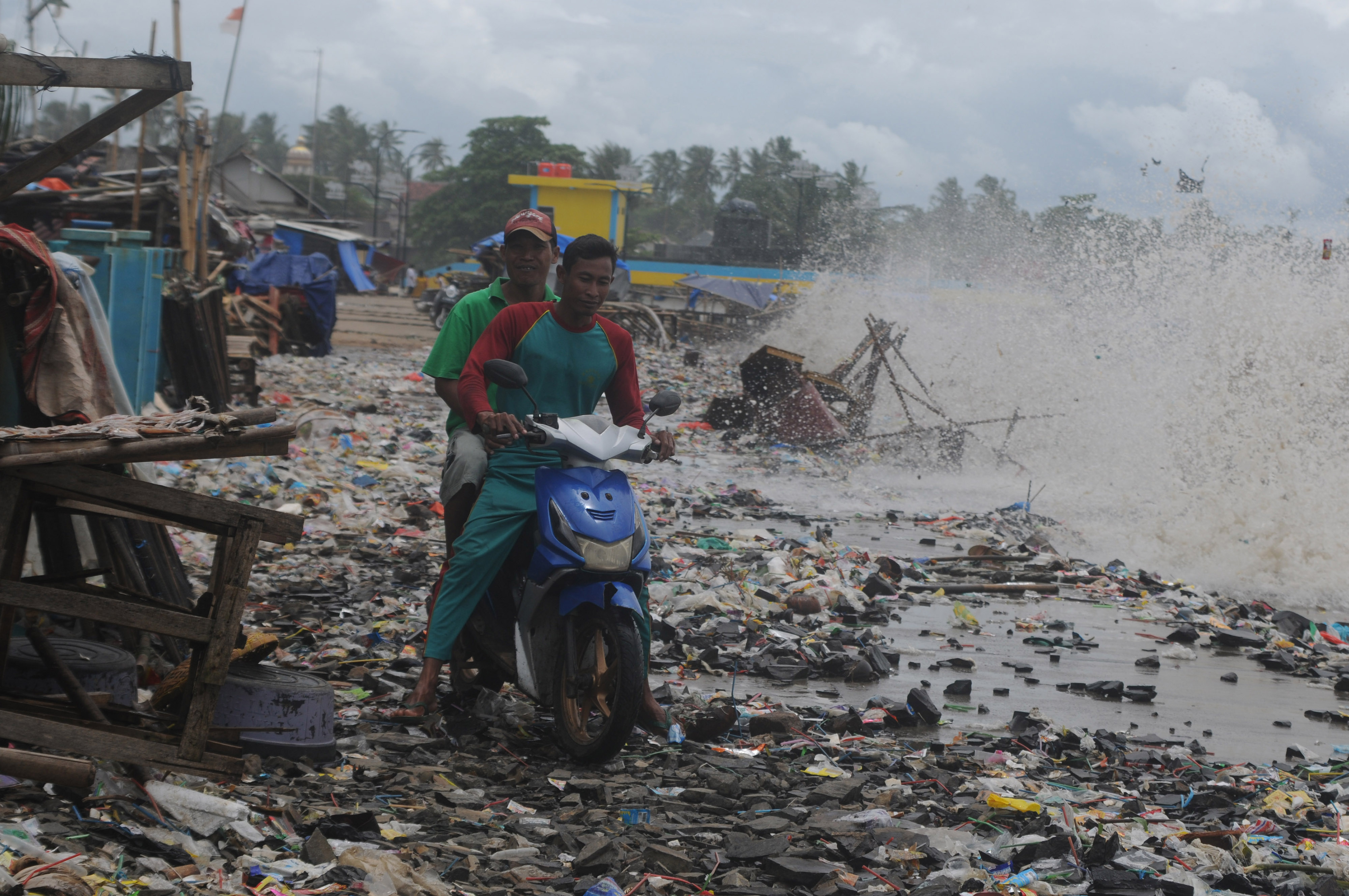 Pengendara roda dua melintasi tumpukan sampah yang terbawa ombak di Teluk Labuan, Pandeglang, Banten, Senin (7/2/2022). 