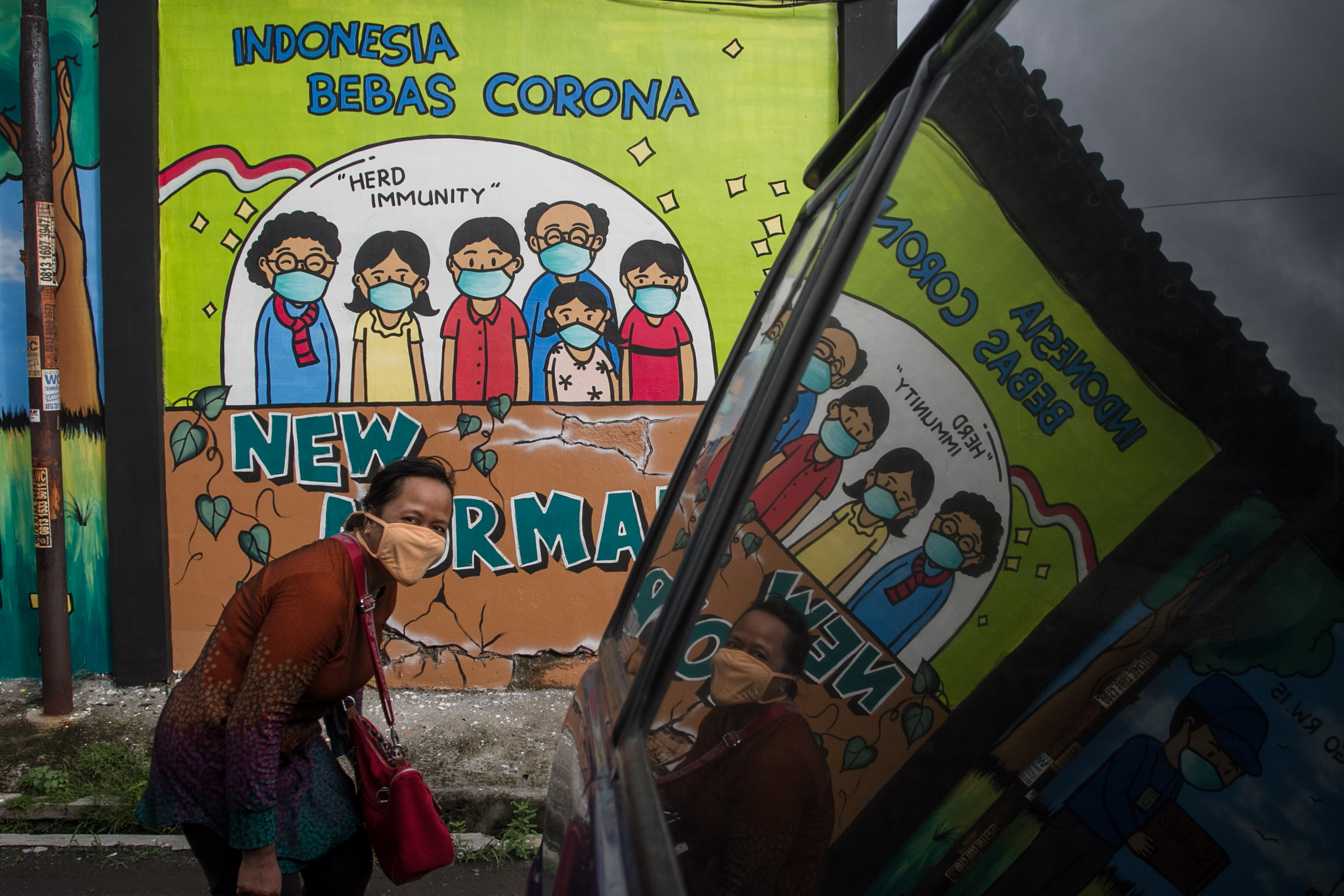 Warga berjalan di depan mural bertema penanganan COVID-19 di Mojosongo, Solo, Jawa Tengah, Jumat (12/11/2021).