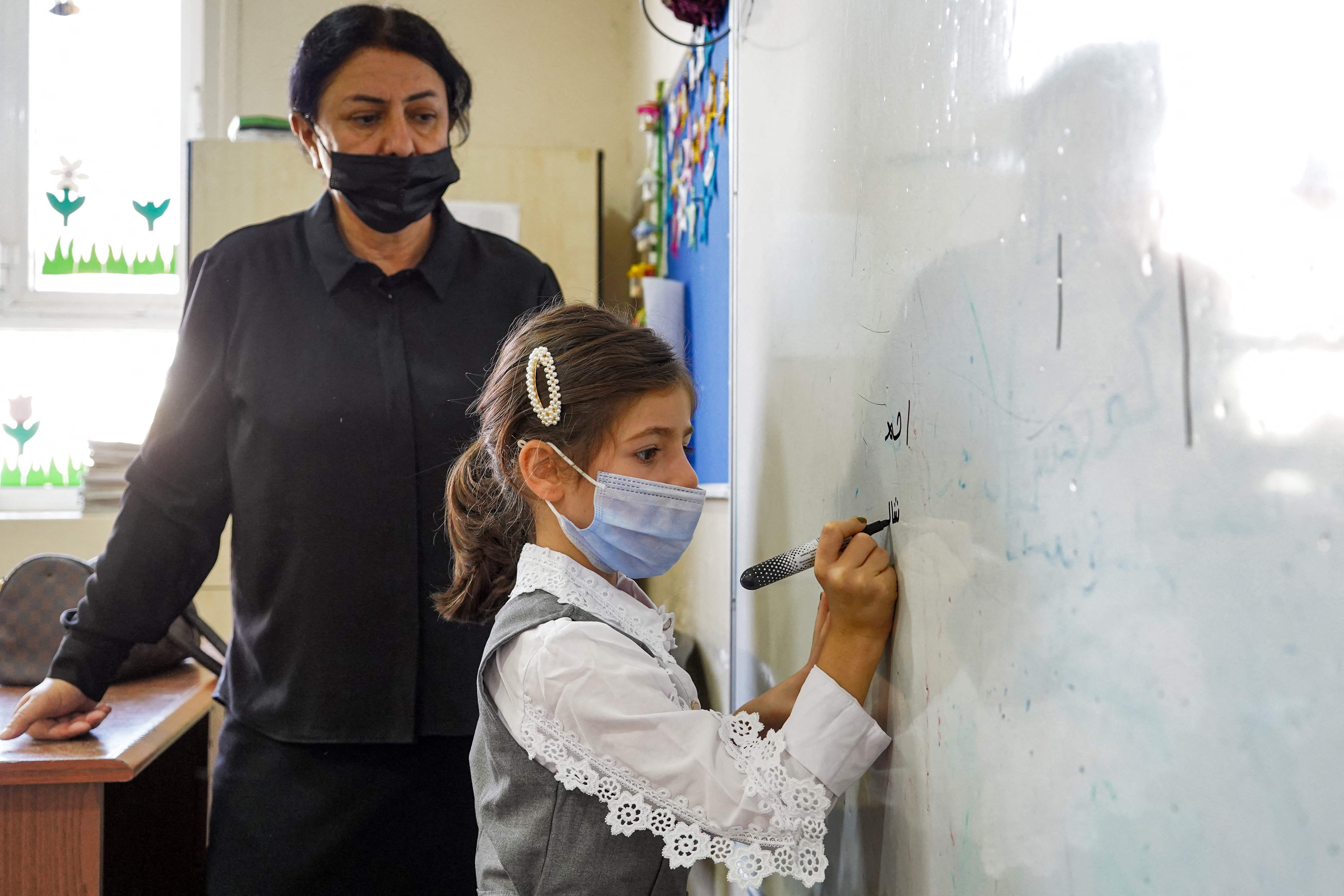 Ilustrasi seorang siswa dengan mengenakan masker menulis di papan berwarna putih.