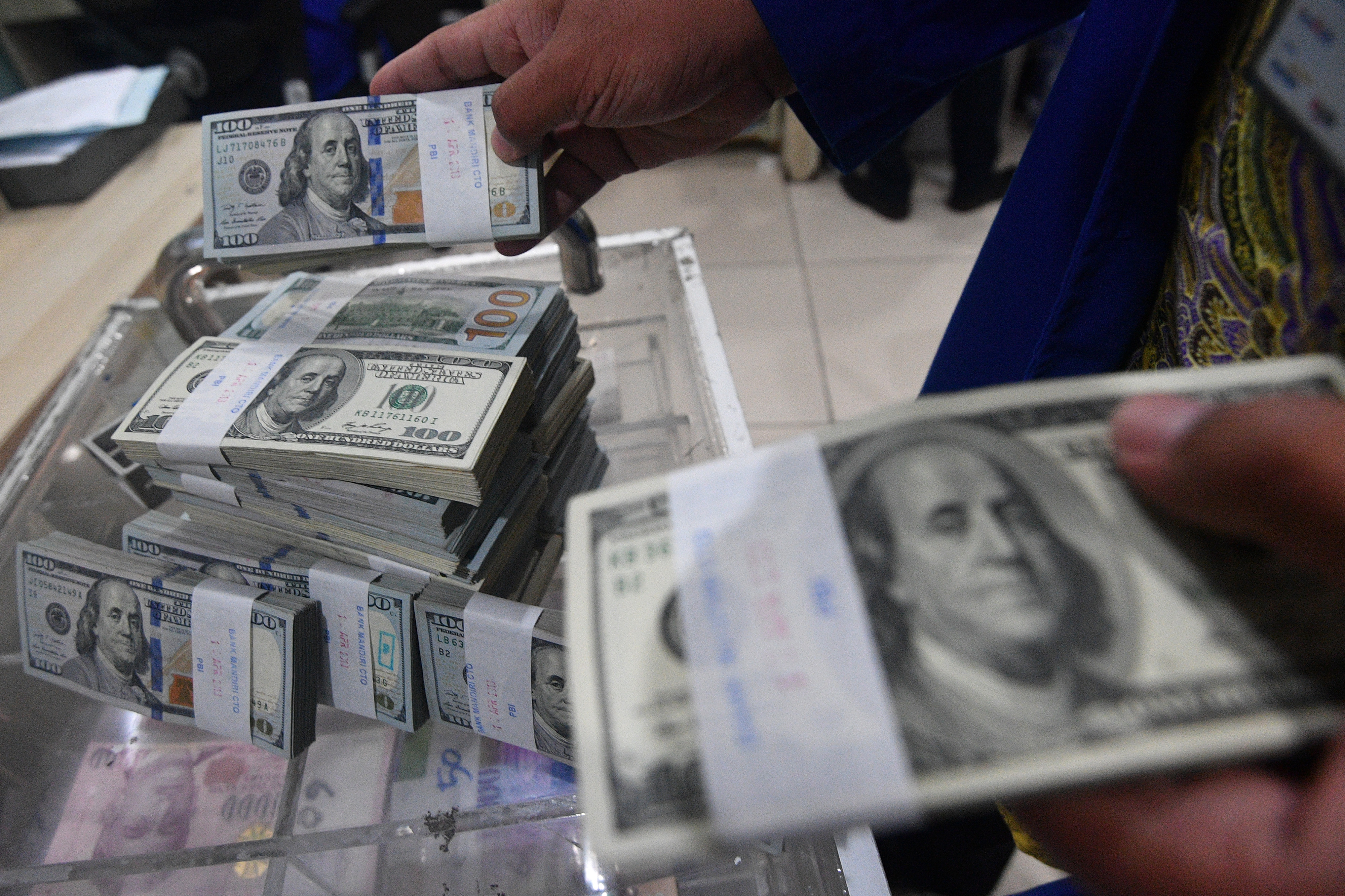 Petugas bank menata tumpukan uang dolar AS.