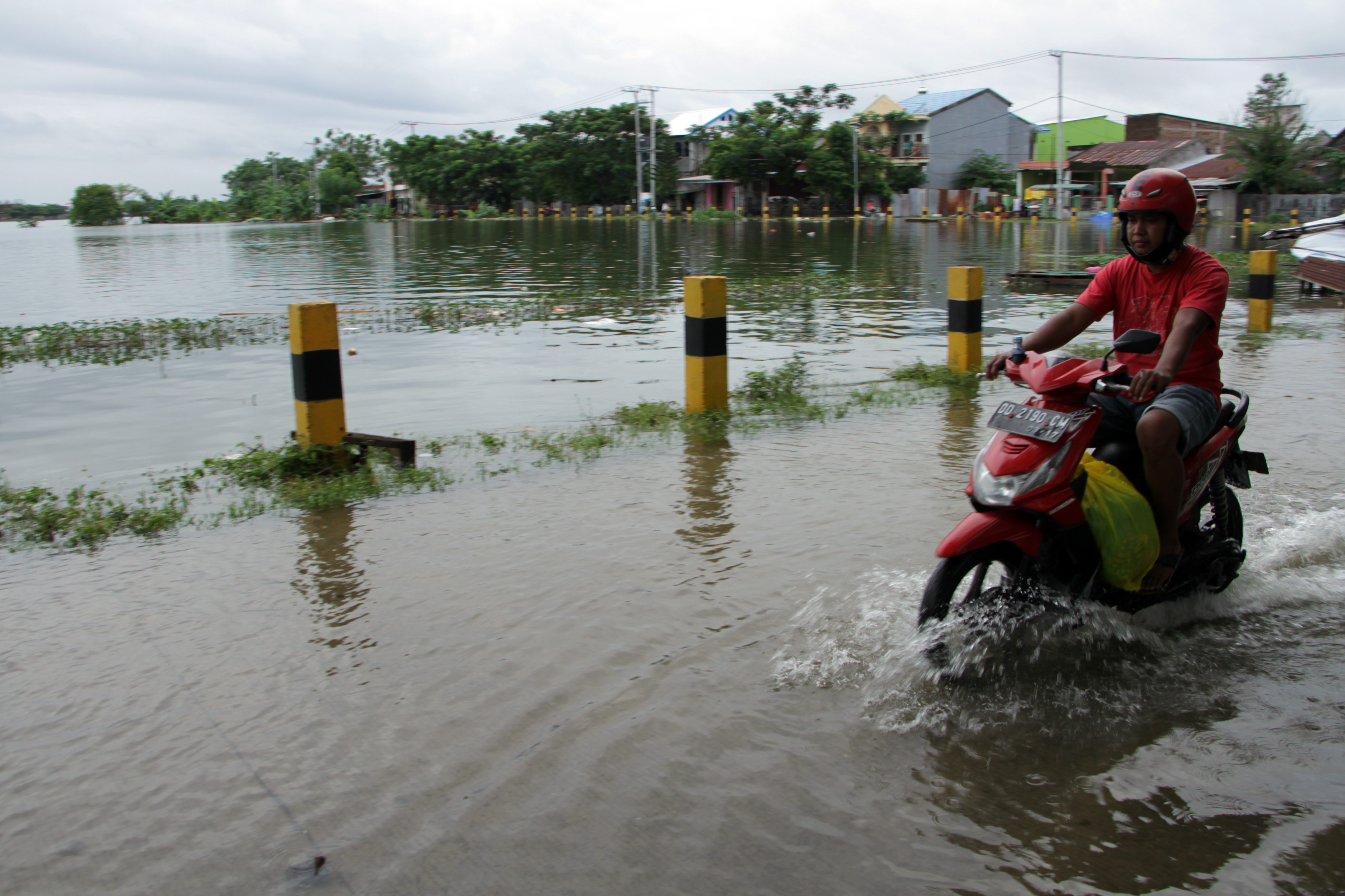 Pengendara motor melintas di pinggir Waduk Tunggu Pampang yang permukaan airnya meluap di Makassar, Sulawesi Selatan, Selasa (7/12/2021)