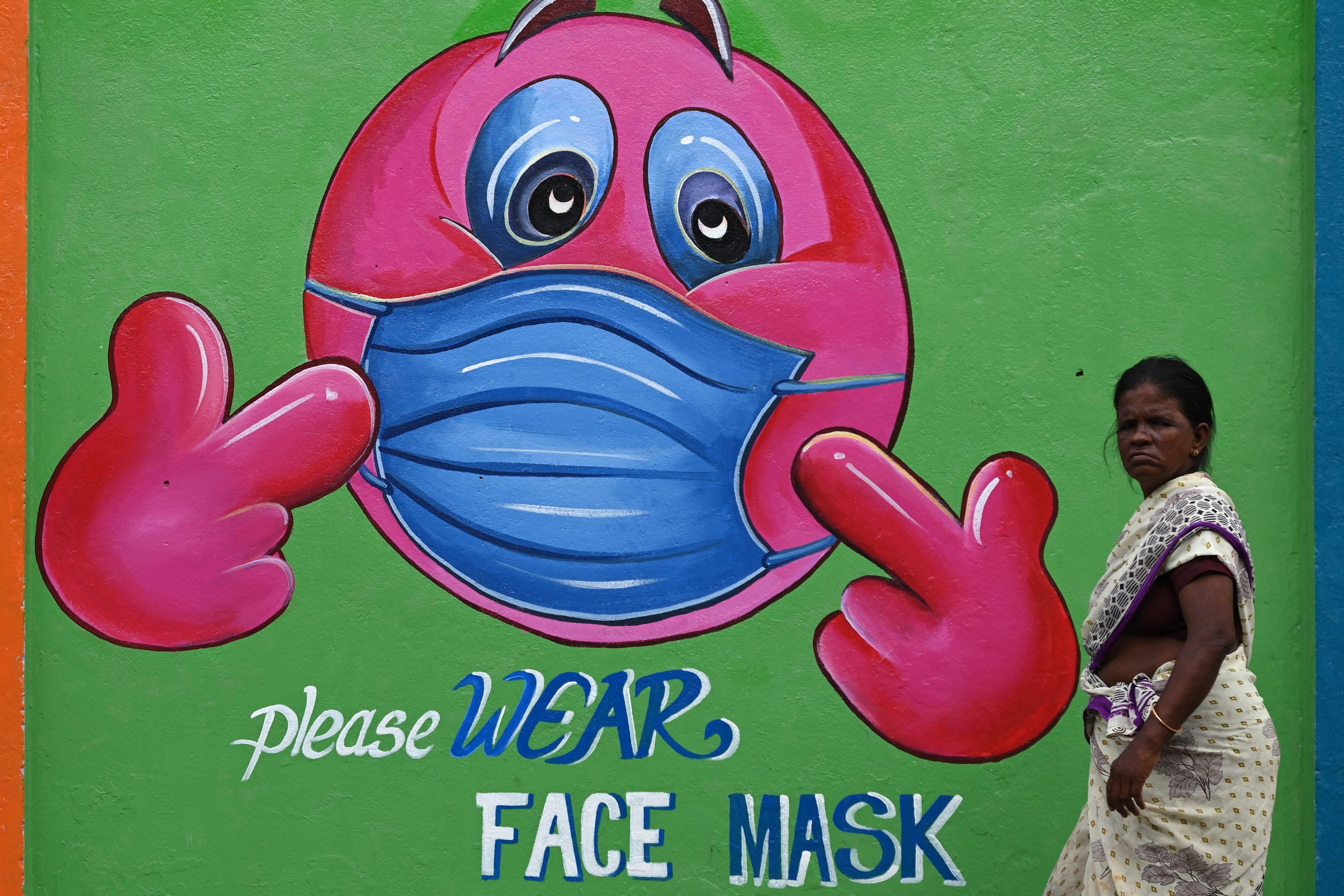 Seorang perempuan melintasi mural terkait pandemi covid-19 di Chennai, India.