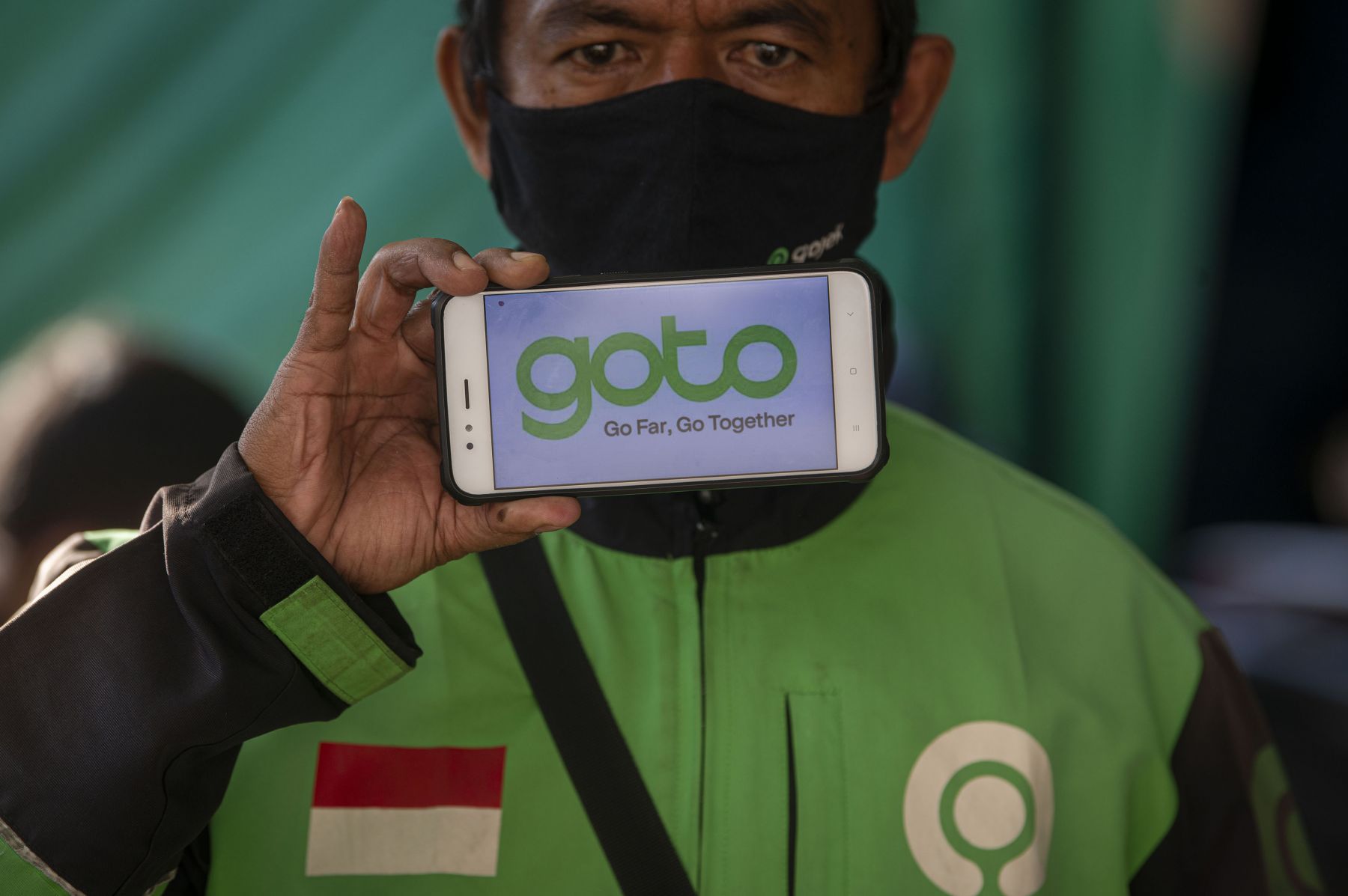 Pengemudi ojek daring Gojek menunjukkan logo merger perusahaan Gojek dan Tokopedia.