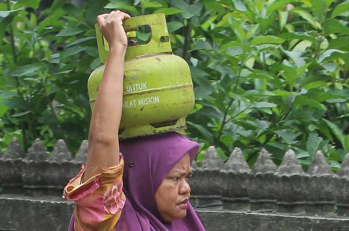 Seorang ibu membawa tabung gas 3 kg di atas kepalanya. 