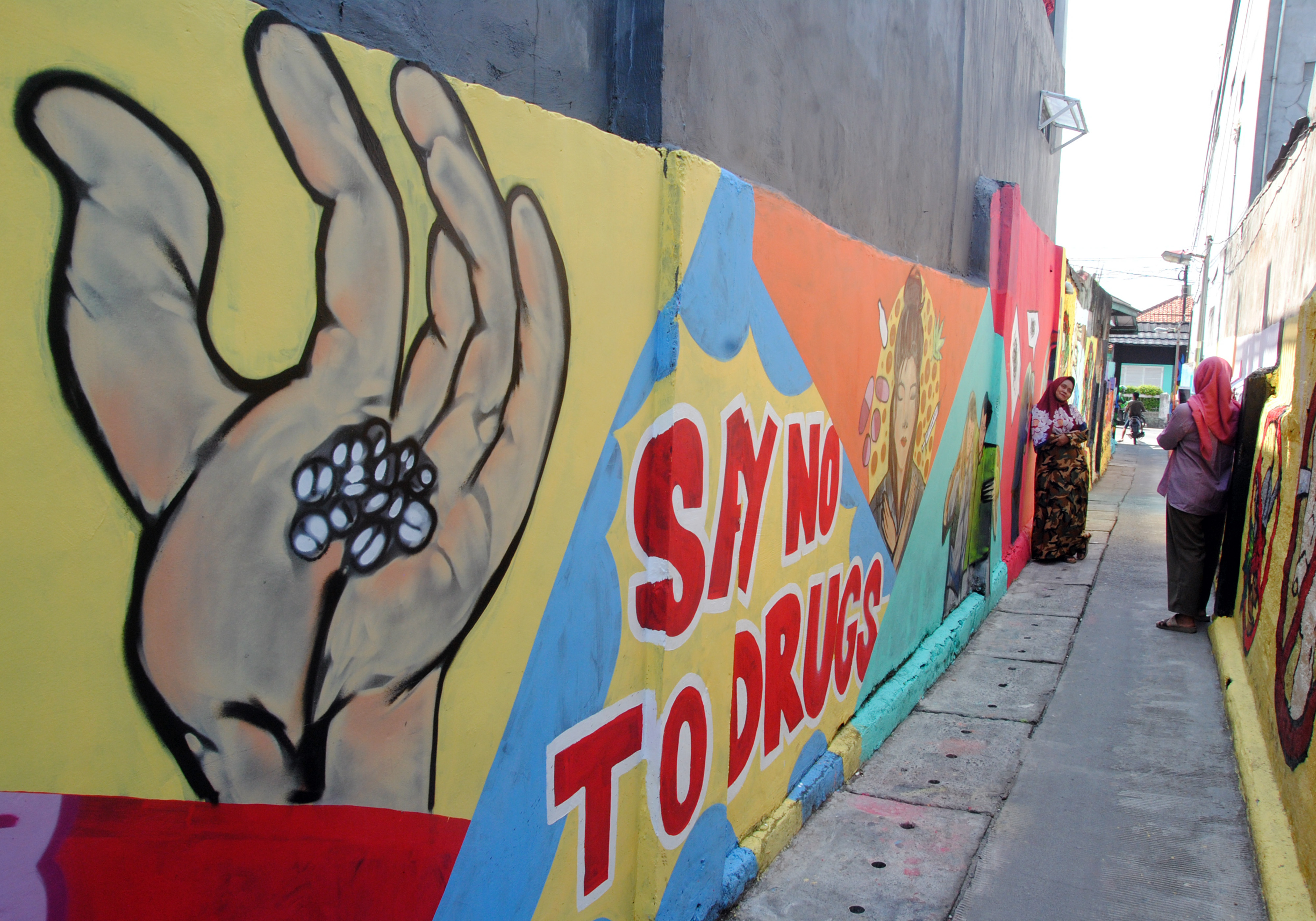 Ilustrasi warga berfoto di depan mural dengan tema antinarkoba.