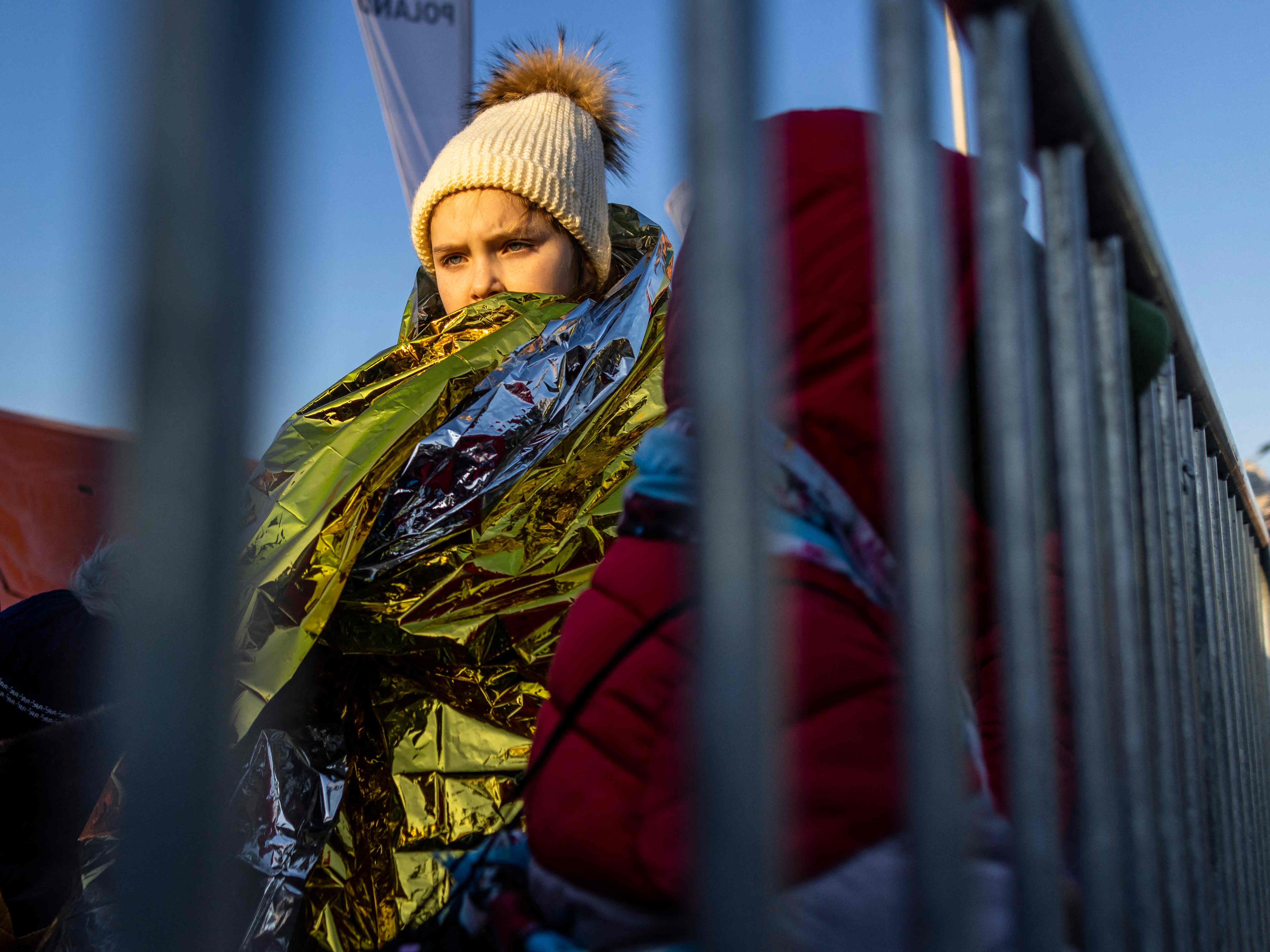 Seorang gadis terbungkus selimut saat dia dan yang lain berbaris untuk naik ke bus usai melintasi perbatasan Polandia-Ukraina.