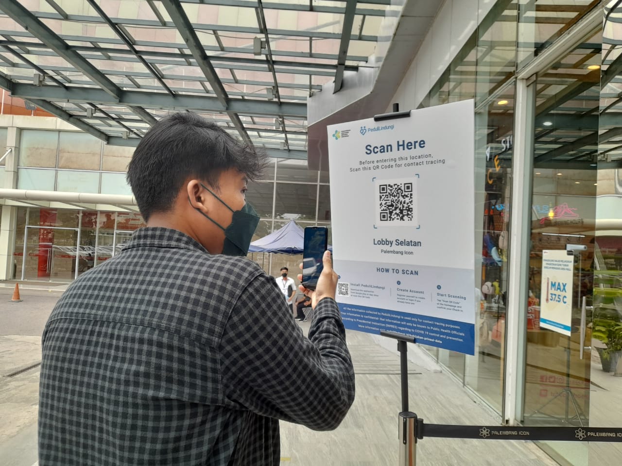 Pengunjung mal Palembang Icon sedang melakukan scan aplikasi PeduliLindungi yang disediakan di pintu masuk mal.