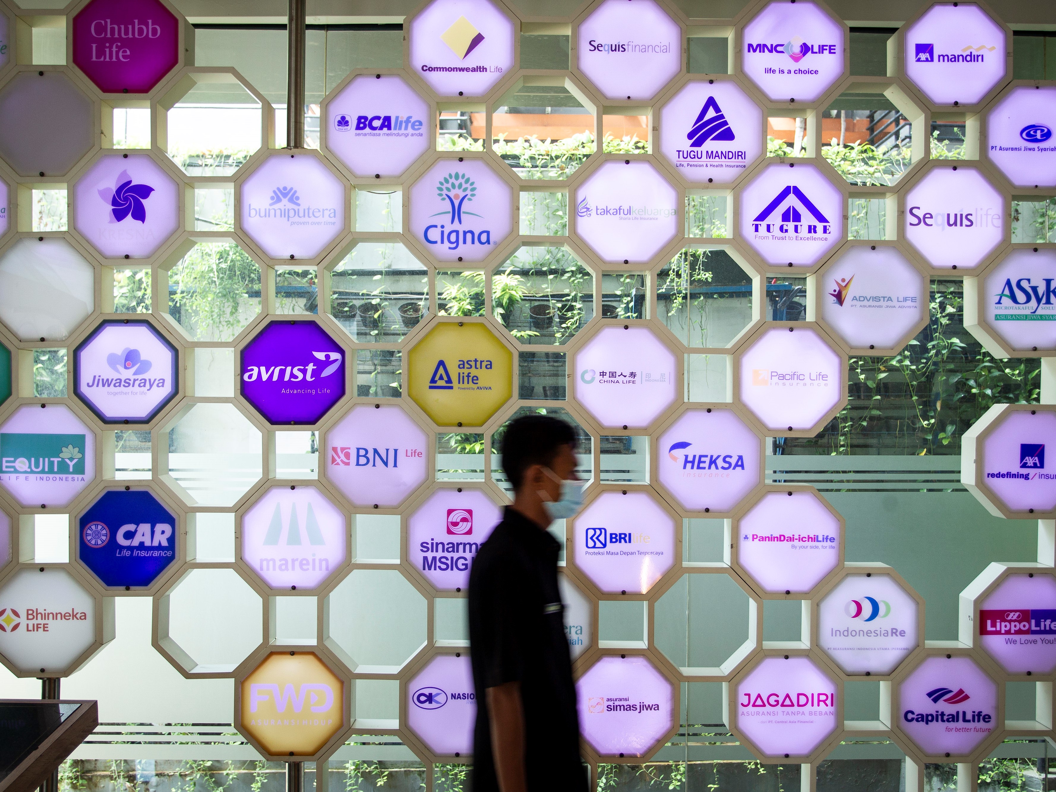 Petugas keamanan berjalan di depan berbagai logo perusahaan asuransi di kantor Asosiasi Asuransi Jiwa Indonesia, Jakarta, Senin (6/7/2020).