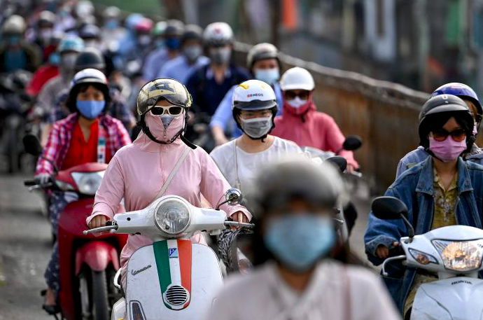 Pengendara sepeda motor mengenakan masker di Hanoi, Vietnam.
