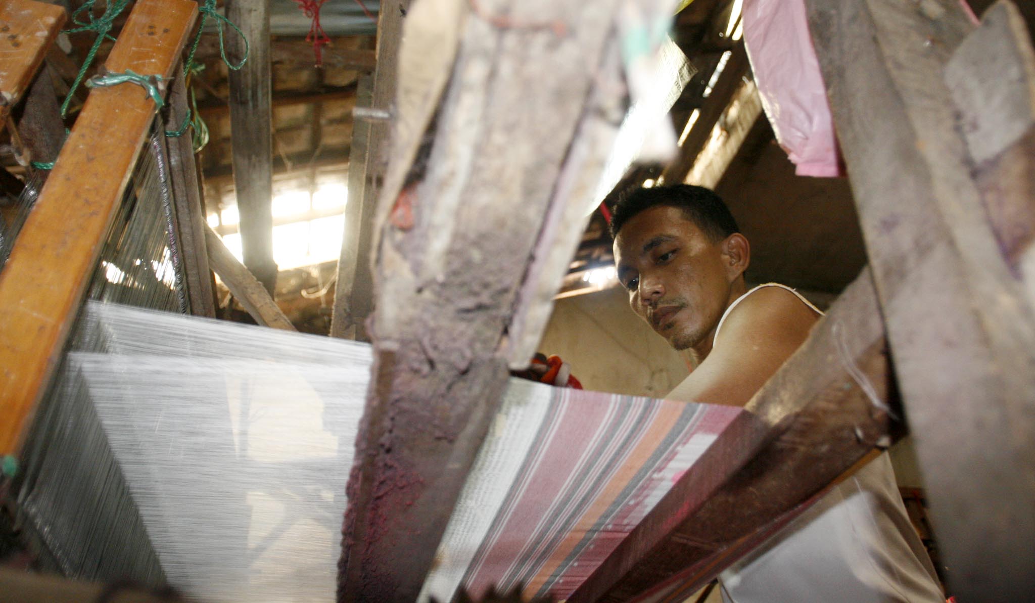 Seorang pekerja melakukan proses menenun kain sarung di sentra tenun ikat Desa Parengan, Kecamatan Maduran, Lamongan