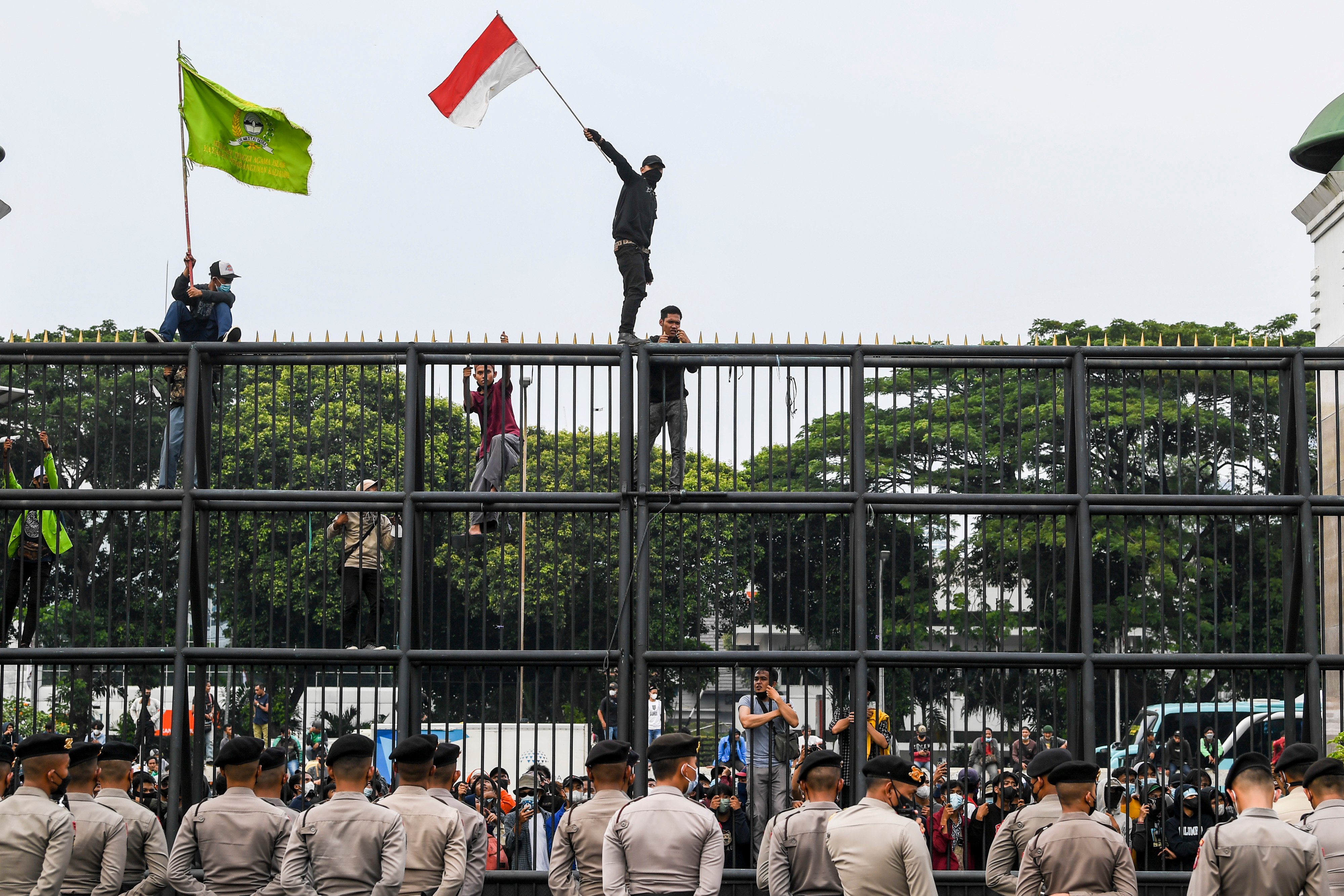 Massa aksi protes mengibarkan bendera Merah Putih dengan menaiki pagar gedung DPR.