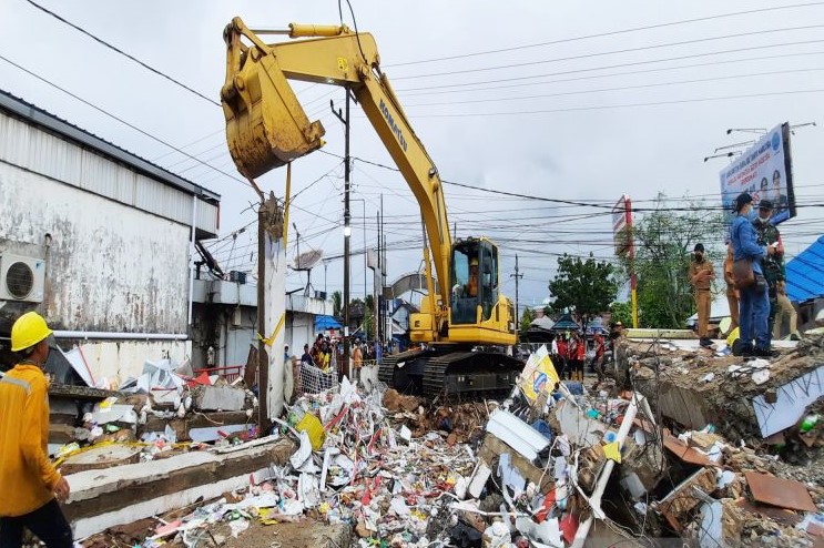 Petugas menggunakan alat berat membersihkan puing-puing rerutuhan bangunan minimarket 