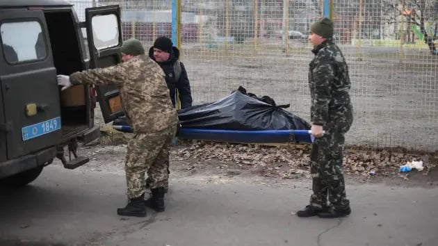 Tiga tentara Ukraina membawa mayat korban tembakan senjata militer Rusia di wilayah utara Kyiv, Ukraina.  