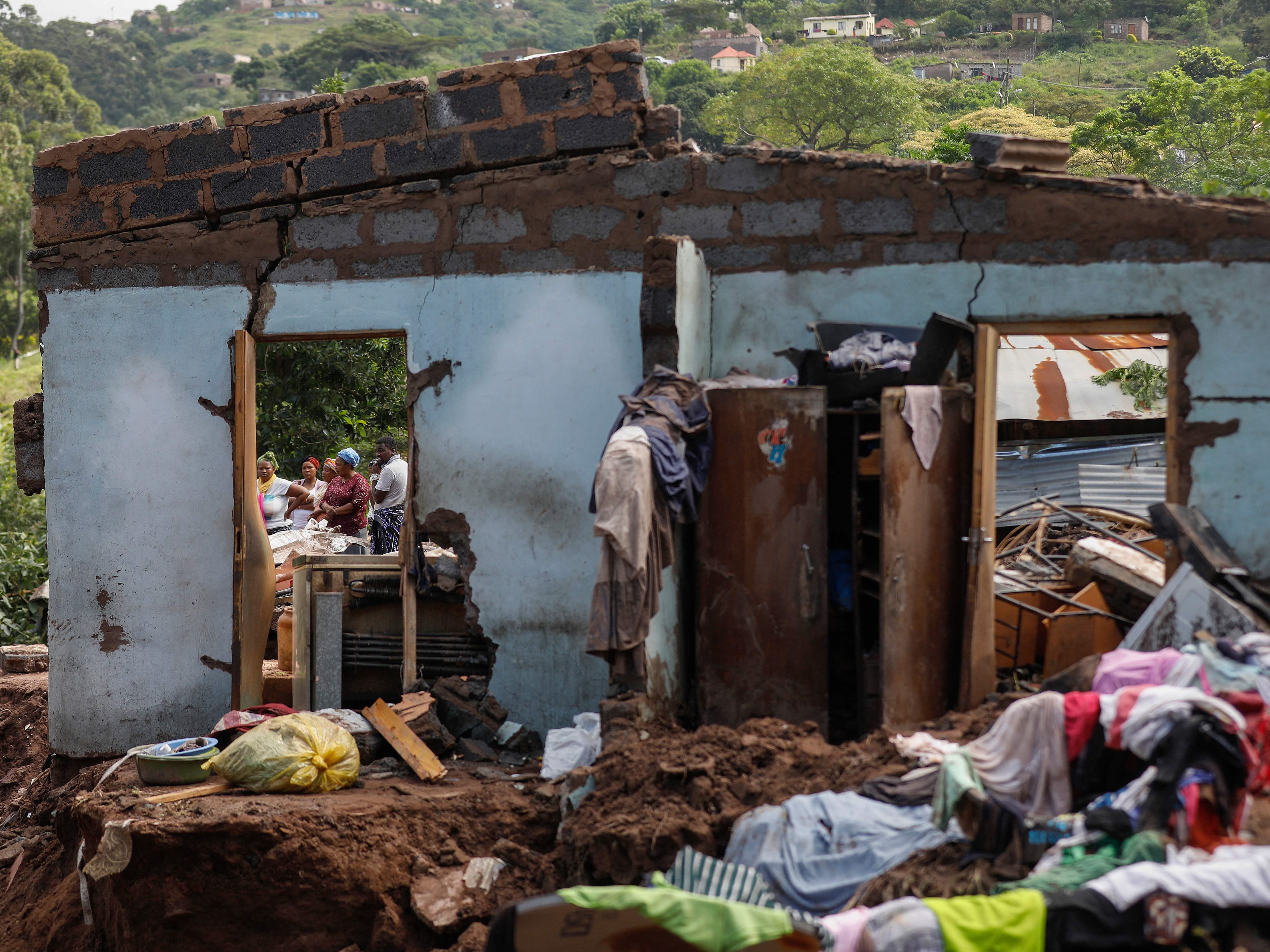 Tetangga berdiri di samping sisa-sisa rumah di kota KwaNdengezi di luar Durban pada 15 April 2022.