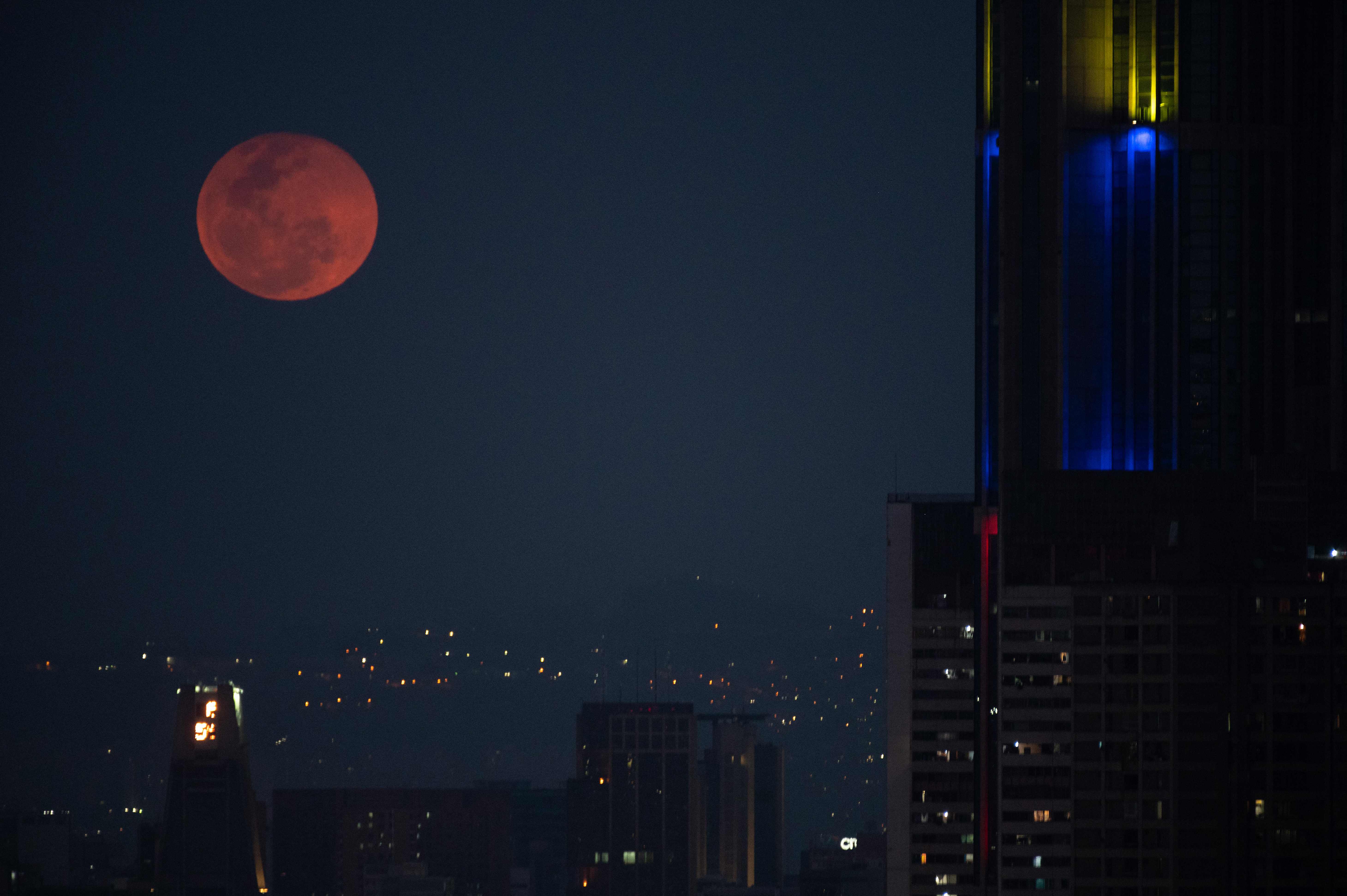Bulan purnama berwarna merah muda terbit di sebelah menara Central Park di Caracas, pada 16 April 2022.