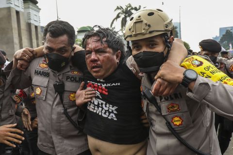 Dua polisi tengah mengevakuasi Ade Armando dari amukan massa