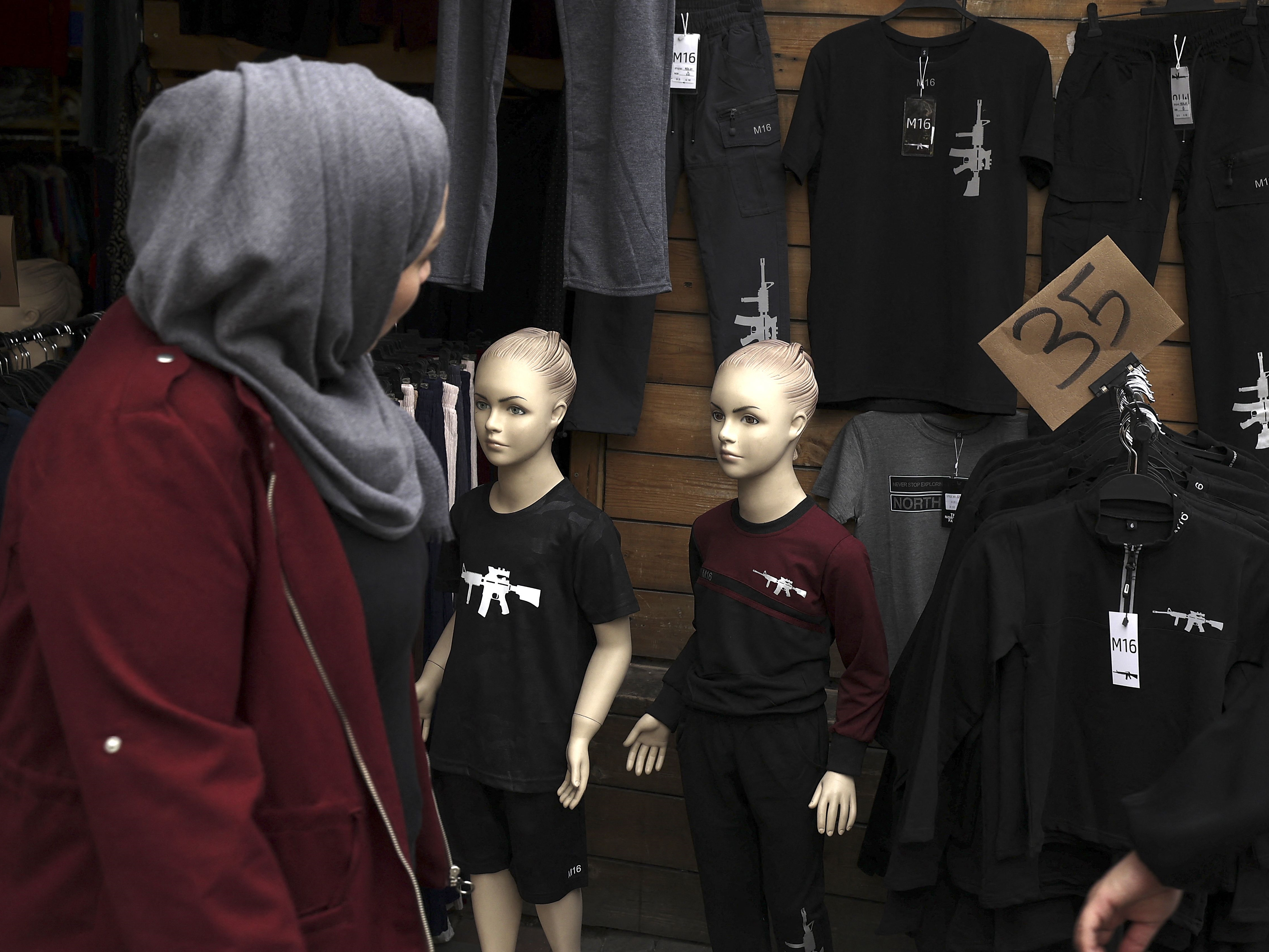 Seorang wanita melihat t-shirt dengan gambar senapan M16 dipajang di etalase toko, pasar kota Ramallah, Tepi Barat.