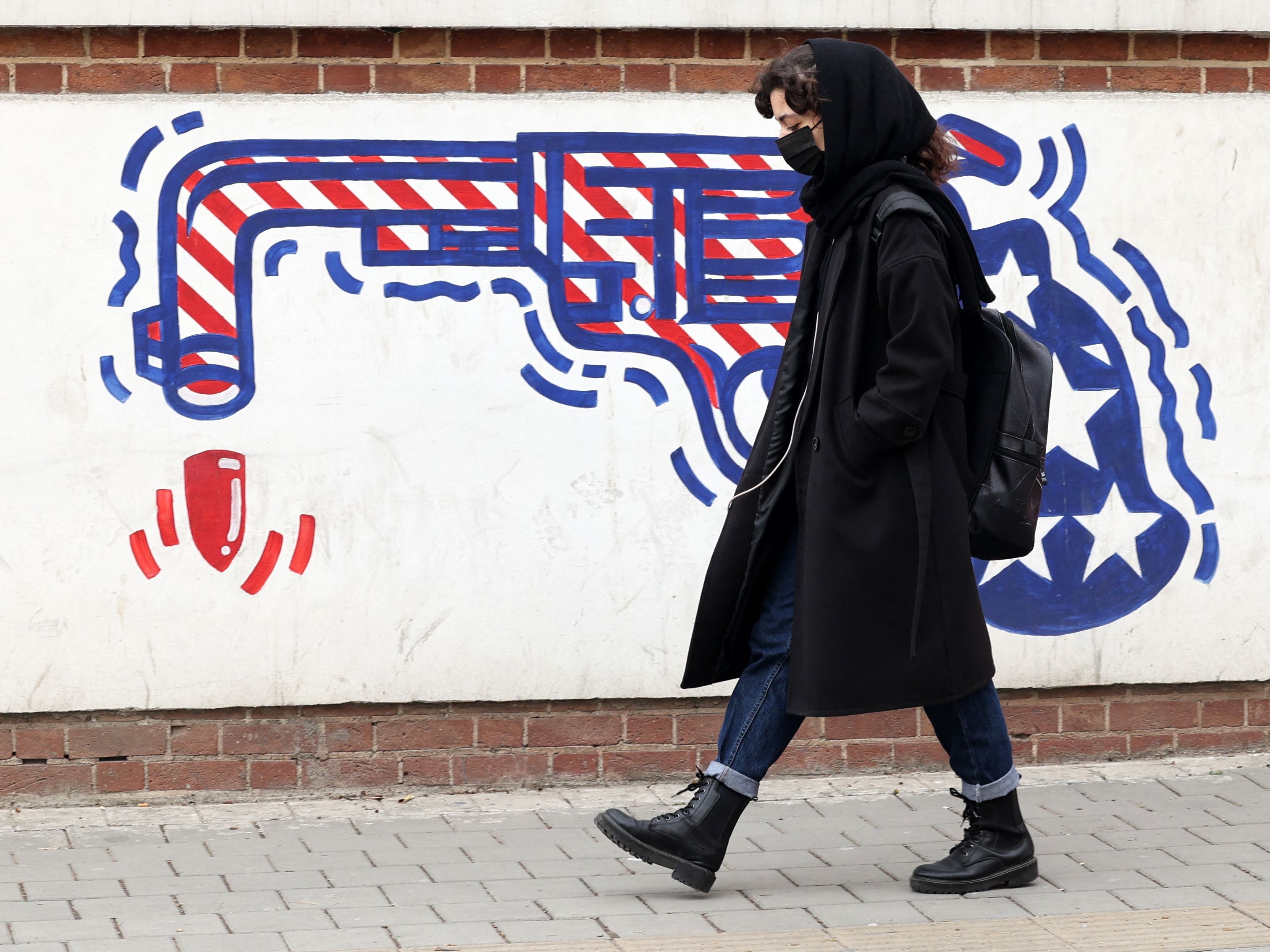 Seorang wanita Iran berjalan melewati mural anti-AS di dinding bekas kedutaan besar Amerika Serikat, Teheran, pada 12 Maret 2022. 