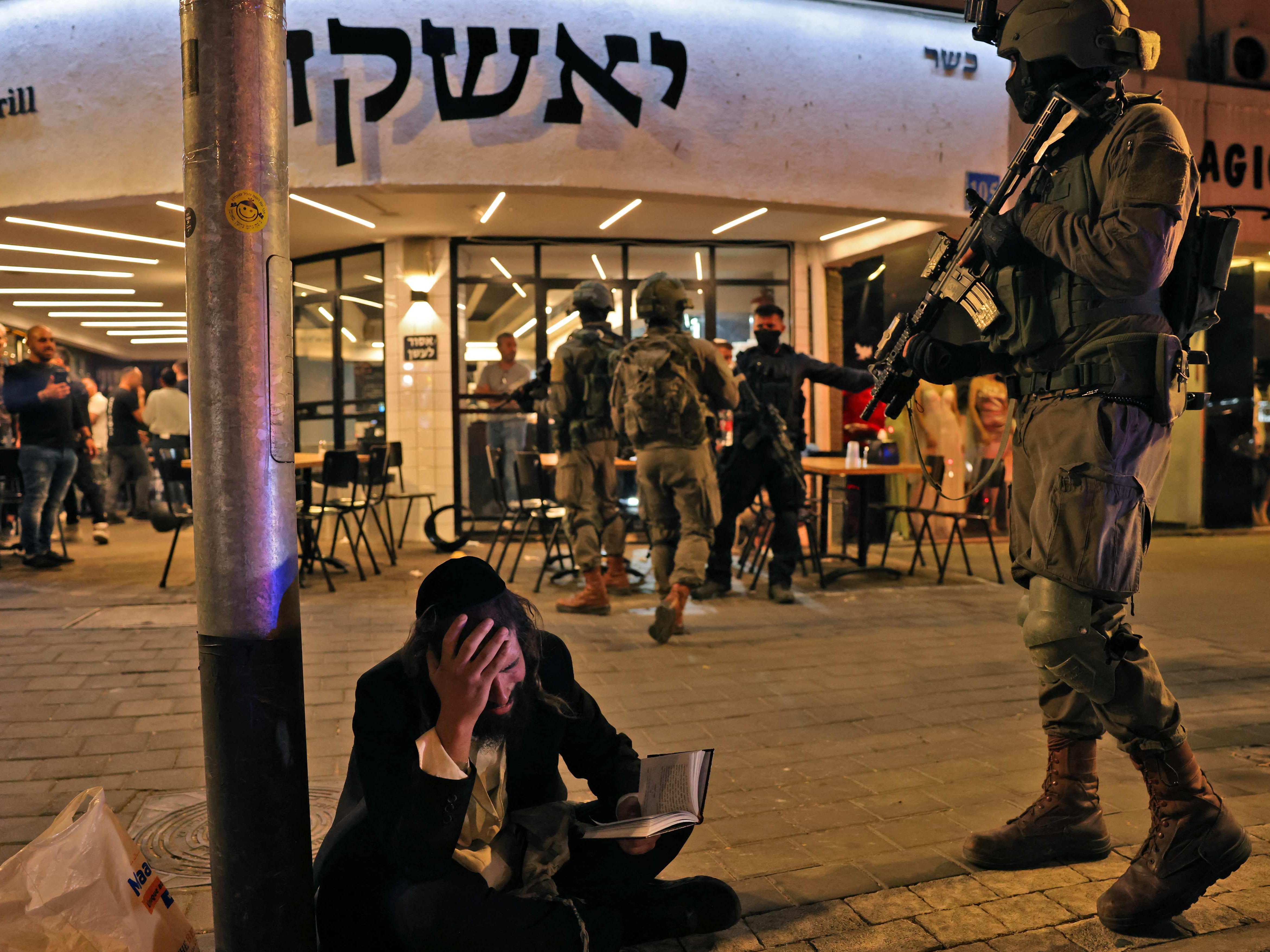 Seorang pria Yahudi ultraortodoks bereaksi sambil memegang satu volume Kitab Mazmur sementara pasukan keamanan berkumpul.